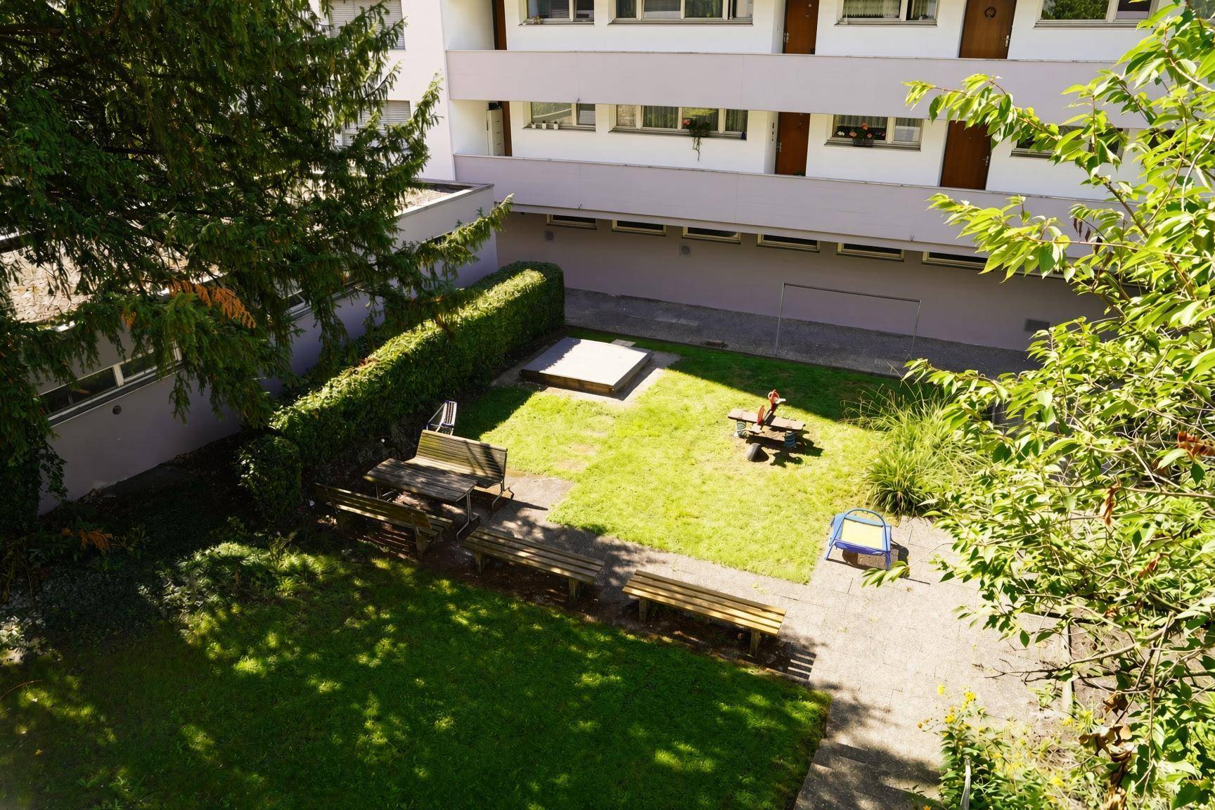 Gemeinschaftsgarten mit Rasenfläche, Bänken und Kinderspielplatz.