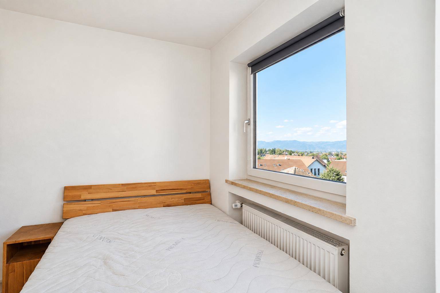 Helles Schlafzimmer mit Holzbett, großem Fenster und Ausblick auf die umliegende Landschaft.