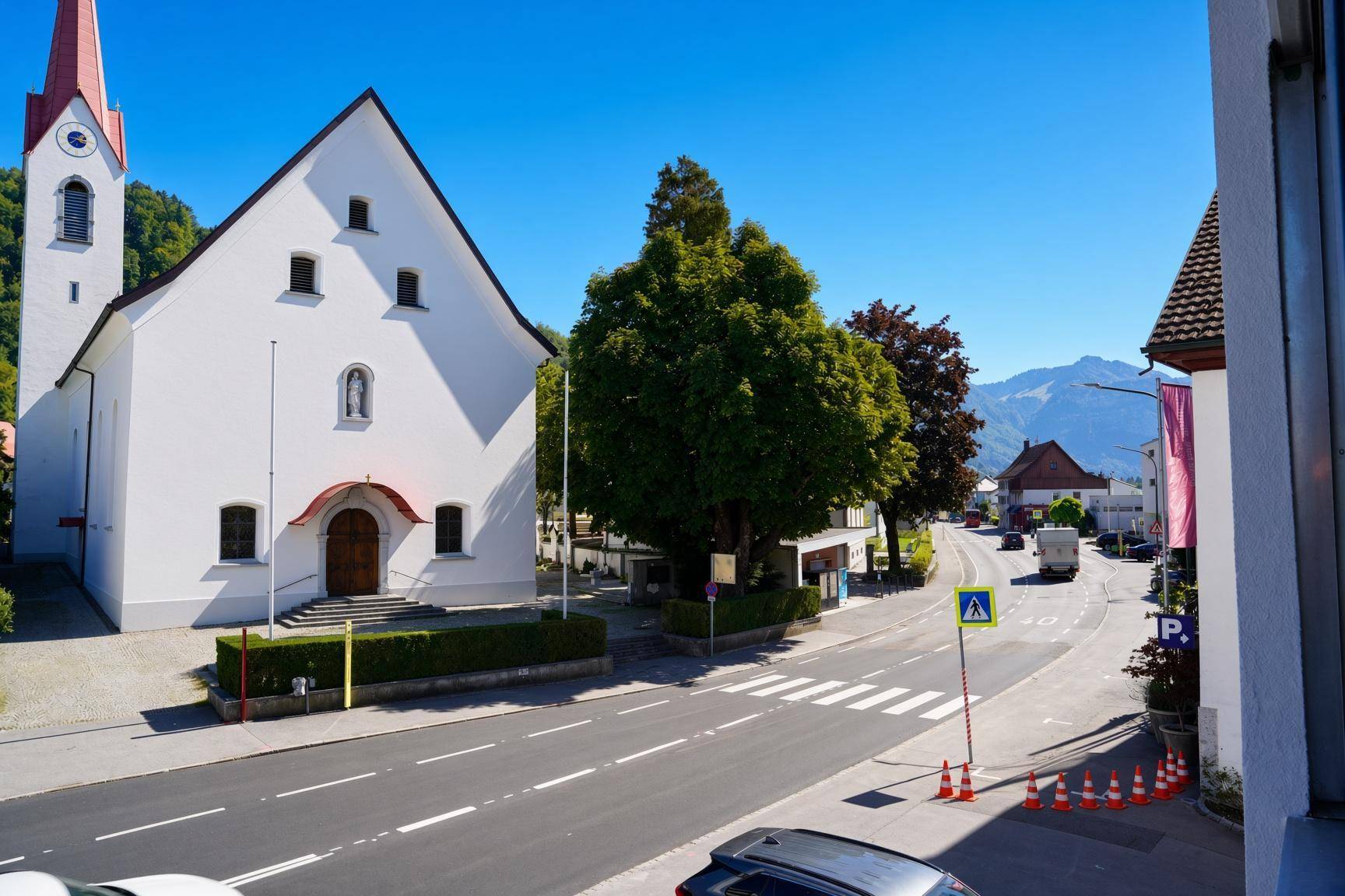 Blick auf eine malerische Straße mit Kirche und Bergen im Hintergrund.