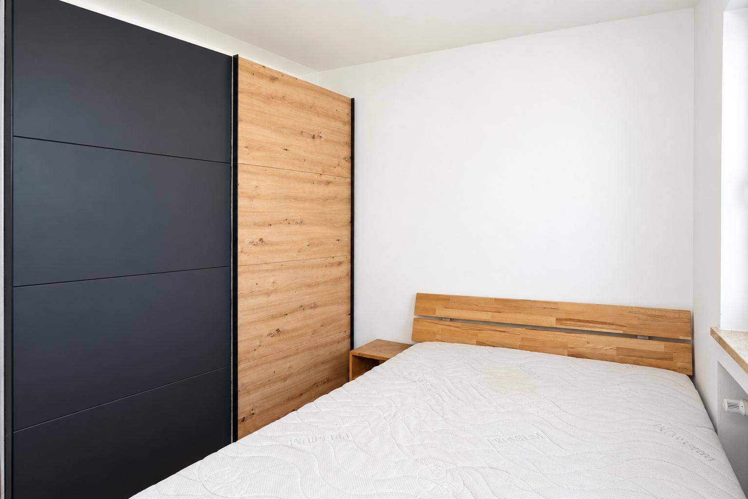 Schlafzimmer mit modernem Holzbett und integriertem Kleiderschrank in Holz- und Anthrazitfarben.