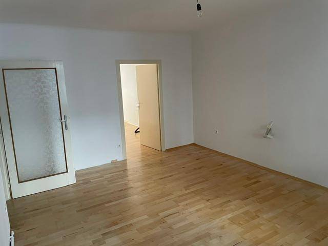 Geräumiges Wohnzimmer mit Parkettboden und Zugang zu weiteren Räumen.