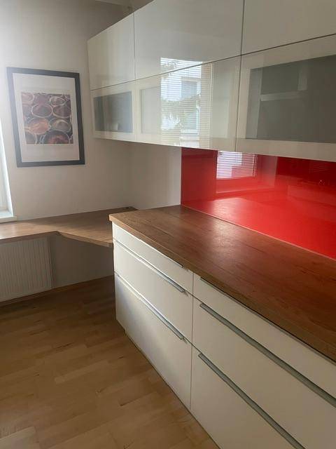 Detailansicht der modernen Küche mit weißen Schränken, roter Rückwand und Holz-Arbeitsplatte.