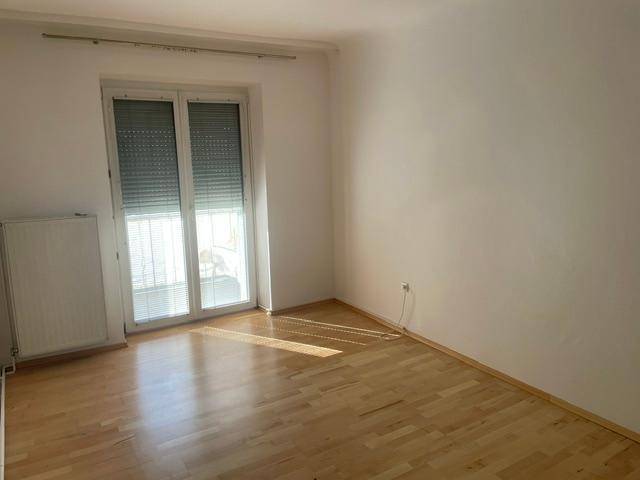 Helles Zimmer mit Parkettboden und großem Fenster mit Rollladen, viel Tageslicht.