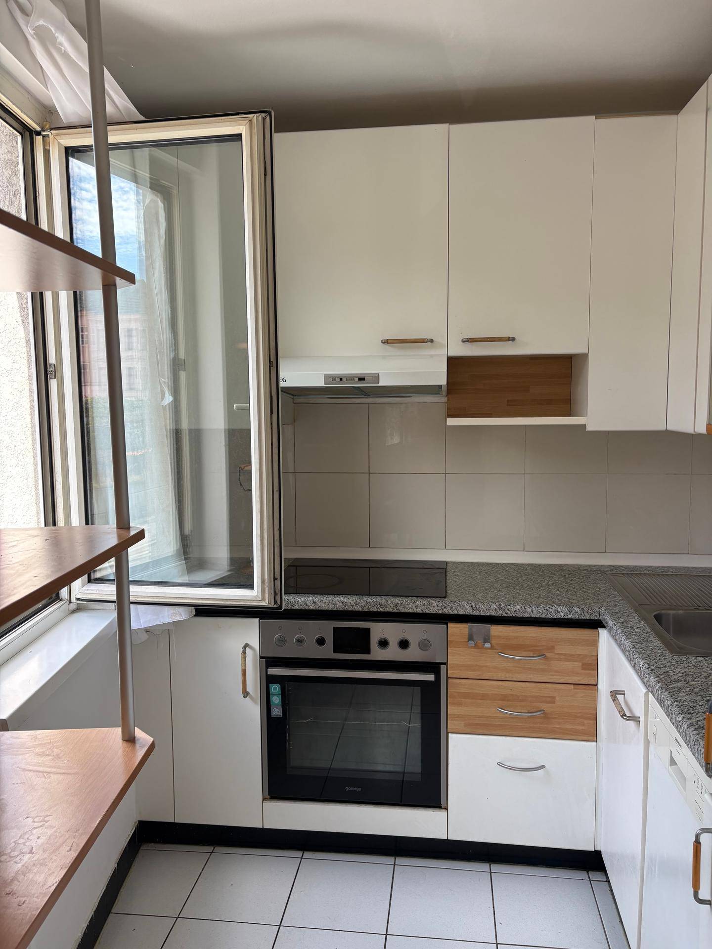 Funktionale Küche mit weißen Schränken, integriertem Backofen und Fenster für natürliches Licht.