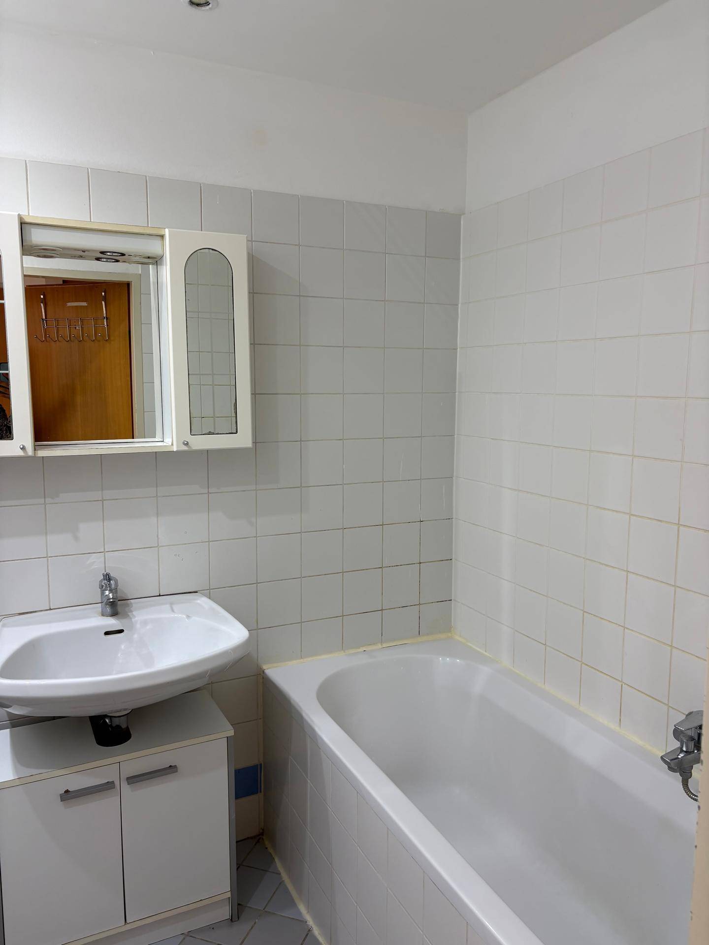 Badezimmer mit Badewanne, Waschbecken und Spiegelschrank, komplett gefliest in hellem Design.