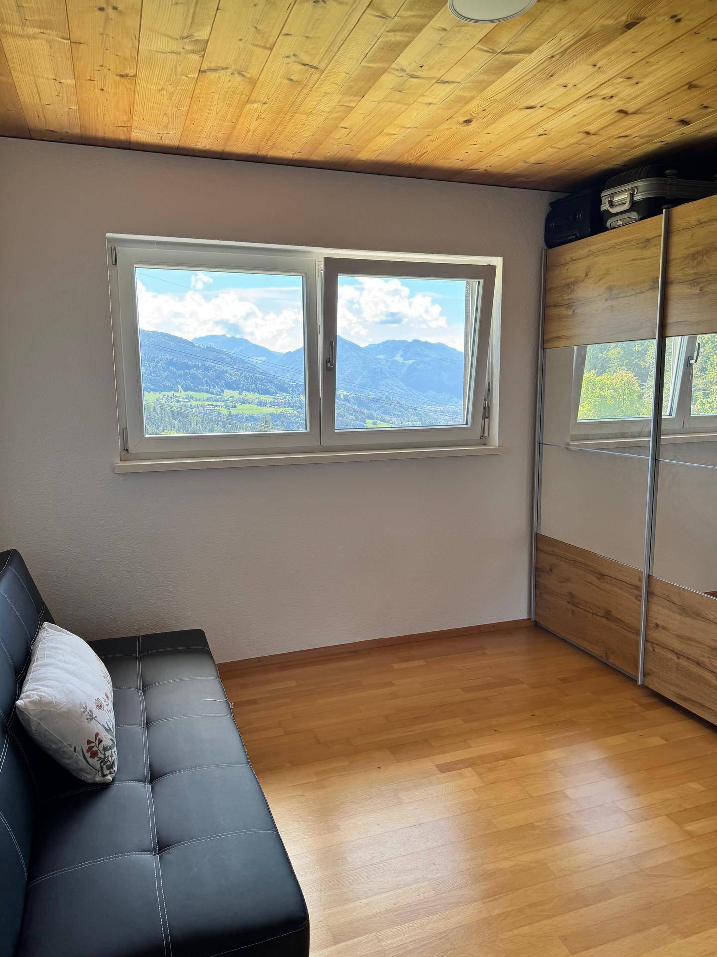 Kleines Schlafzimmer mit Schlafsofa, Spiegelschrank und weitem Blick auf die umliegenden Berge.