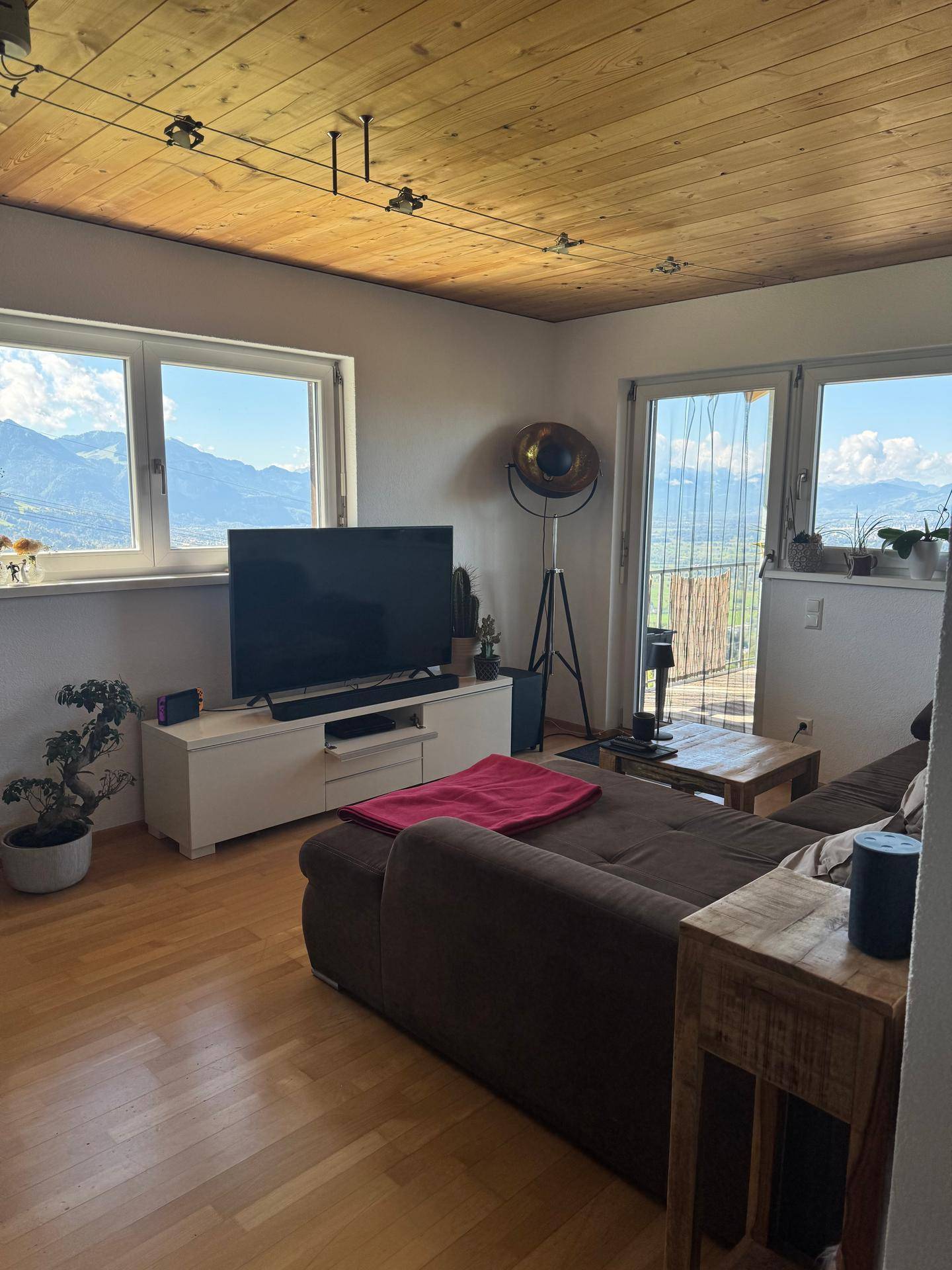 Helles Wohnzimmer mit Holzboden, gemütlichem Sofa und weitem Blick auf die Berge durch große Fenster.