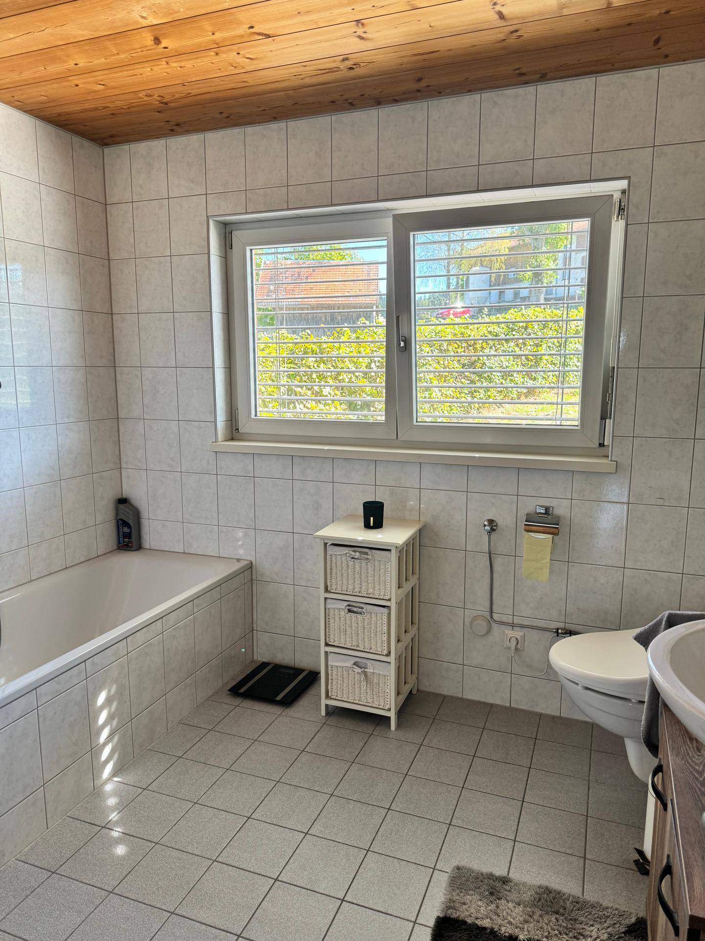 Gefliestes Badezimmer mit Badewanne, Toilette und Fenster für natürliche Belüftung und Licht.