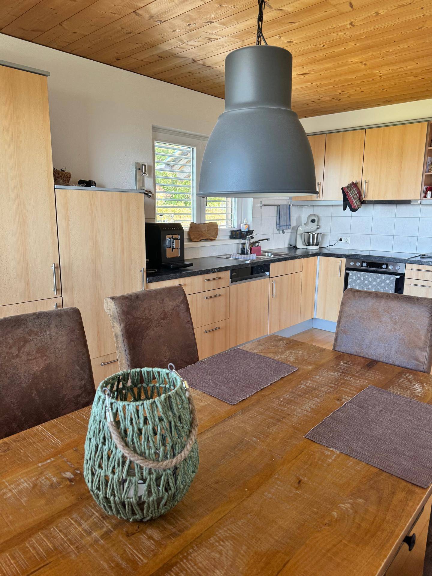 Moderne Einbauküche mit Holzelementen, Esstisch und dunkler Arbeitsplatte unter einer Holzdecke.