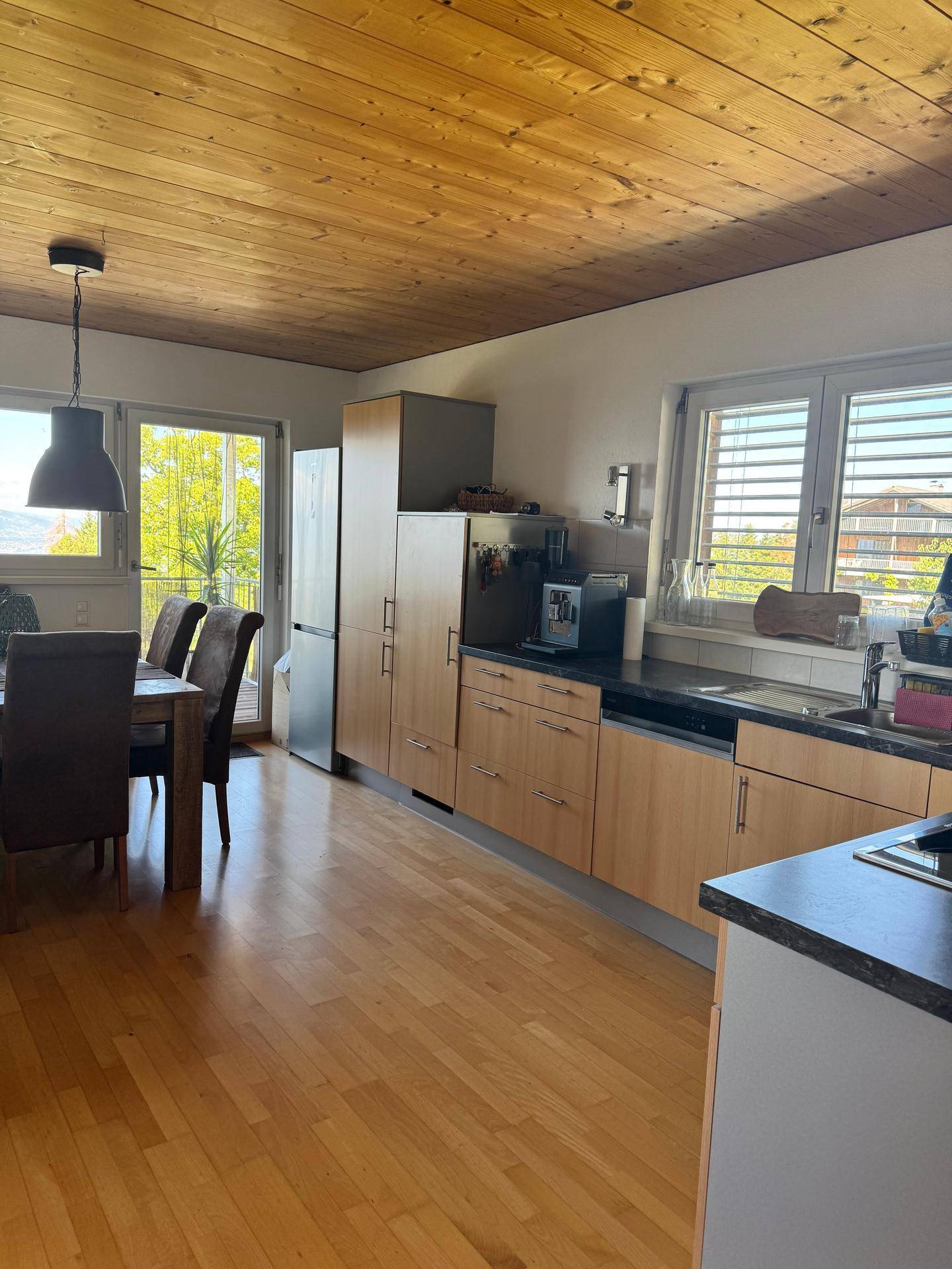 Funktionale Küche mit Essbereich, Holzschränken, Kühlschrank und Zugang zu einem Außenbereich.