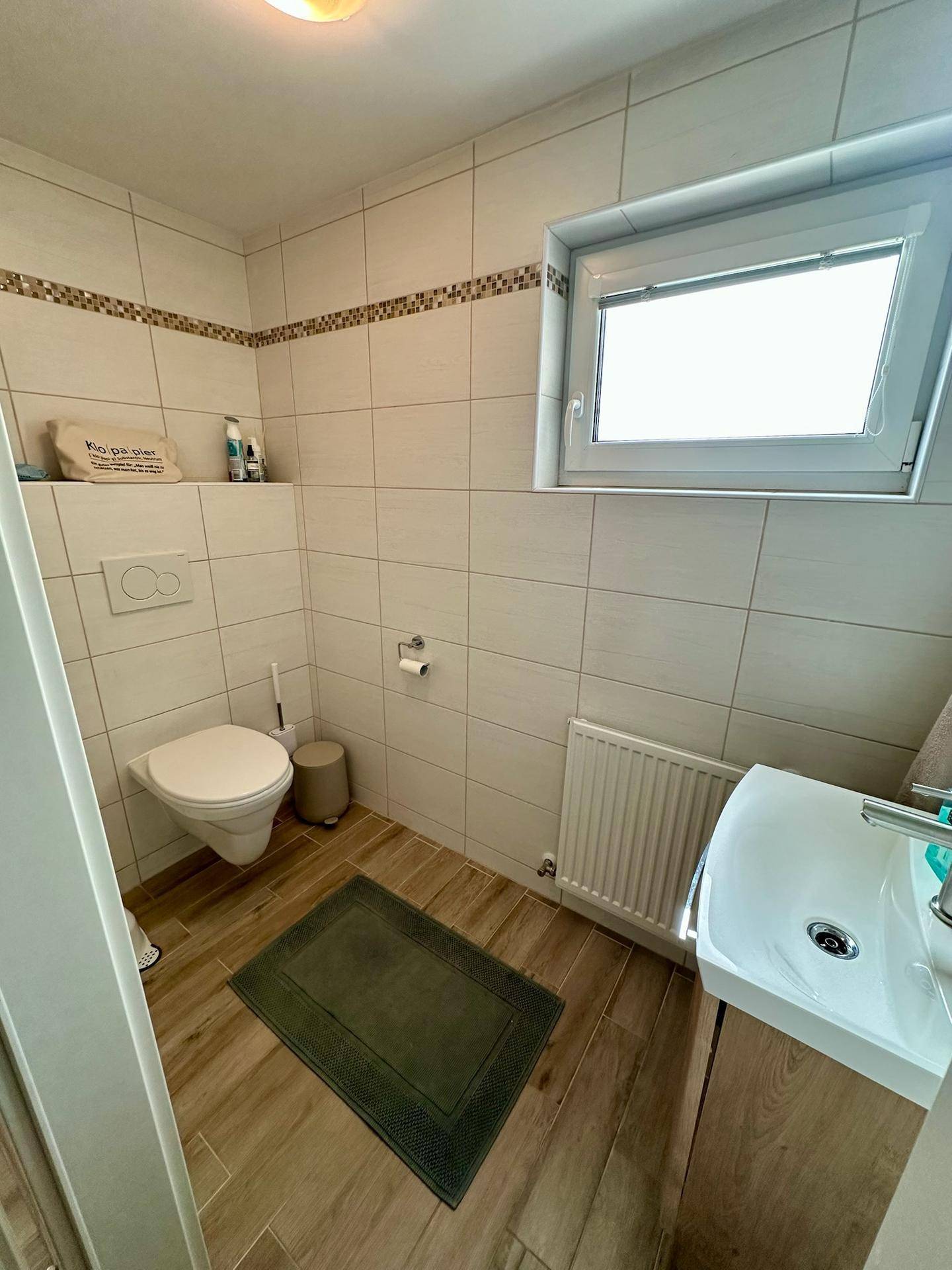 Modernes Gäste-WC mit wandhängendem WC, Waschbecken und Fenster.