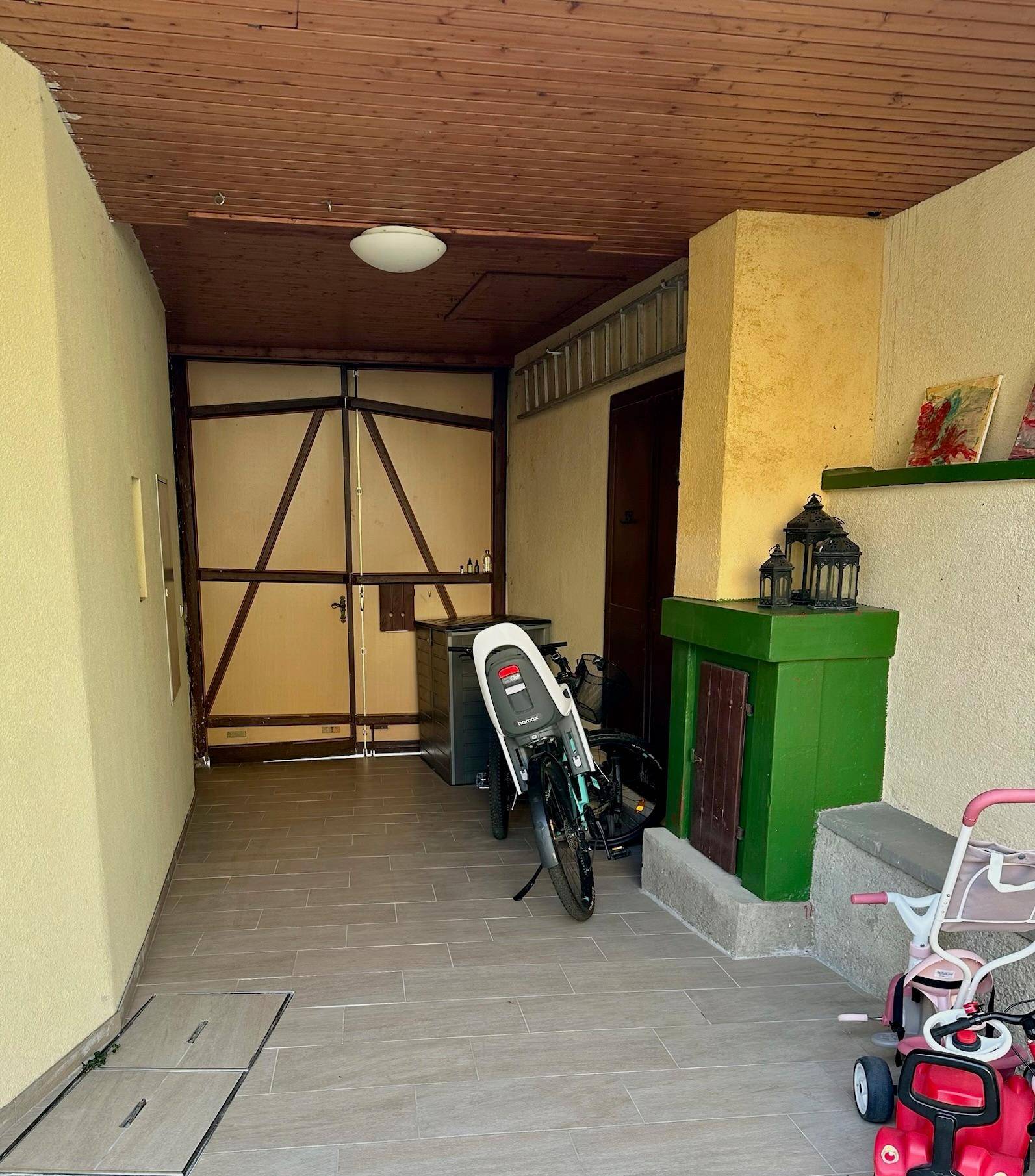Überdachter Bereich mit Holztor, Fliesenboden und Abstellmöglichkeiten.