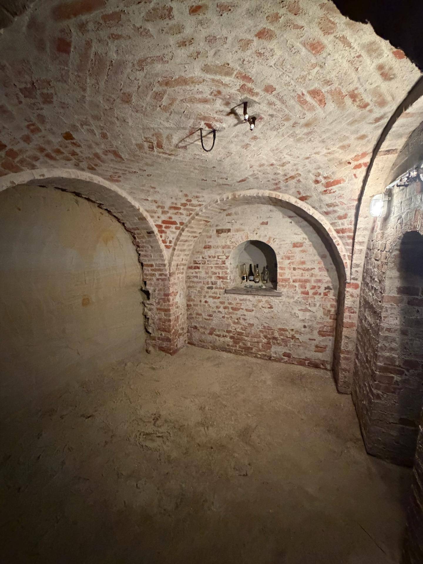 Historischer Kellerraum mit Ziegelgewölbe und Nischen in den Wänden.