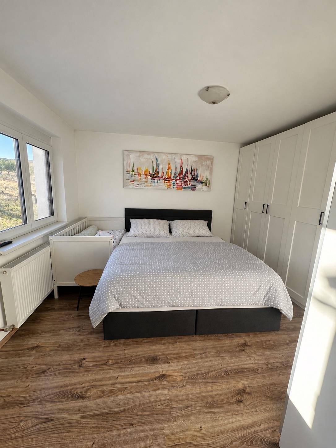 Schlafzimmer mit Doppelbett, weißem Kleiderschrank und Blick ins Grüne.