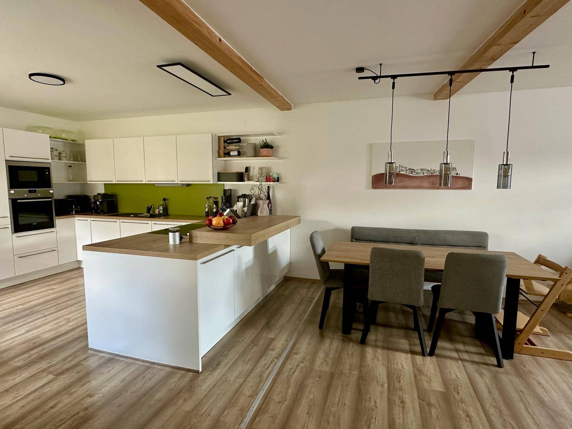 Moderne offene Küche mit weißer Hochglanzfront, Holztheke und Essbereich.