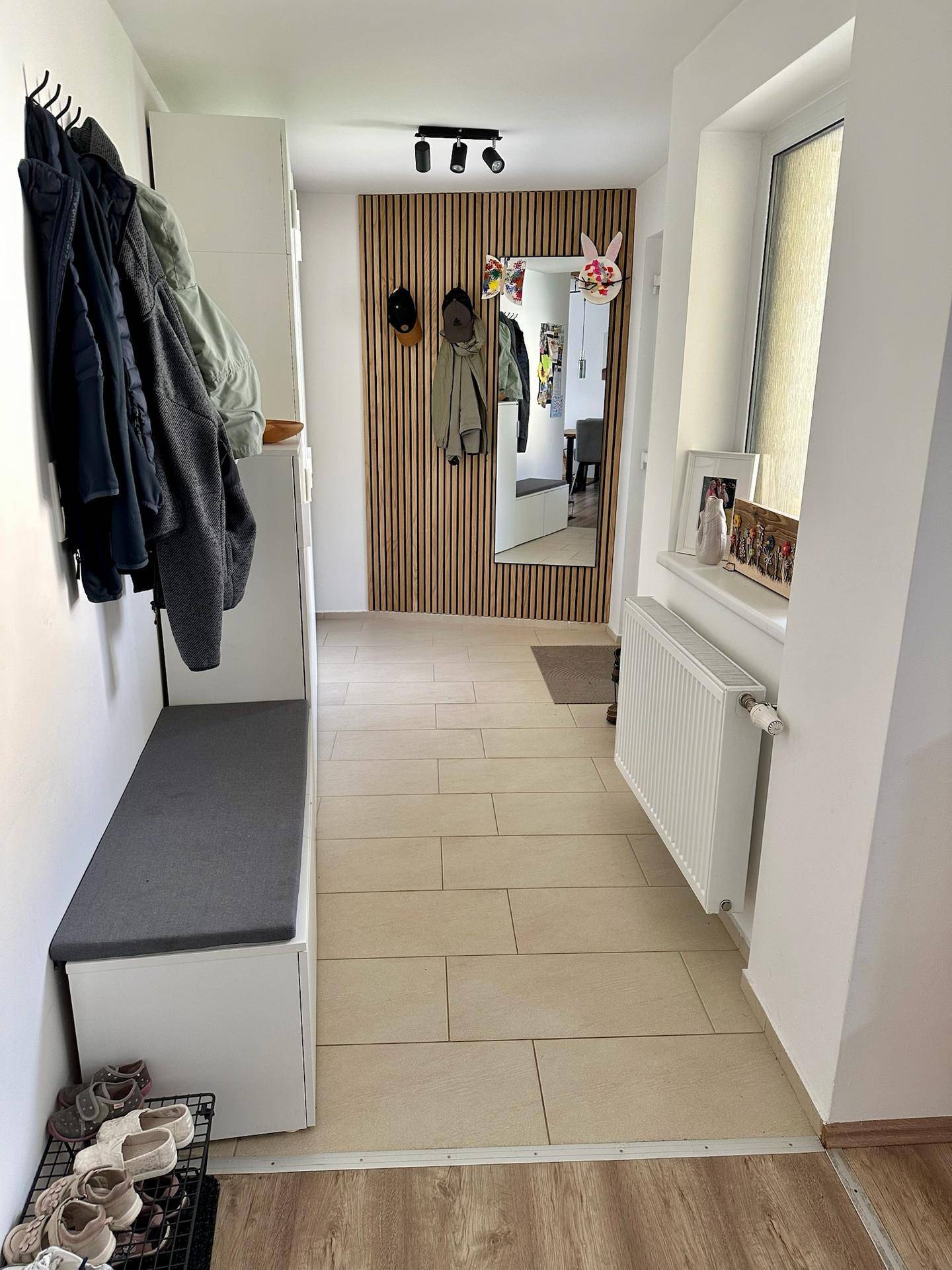 Moderner Eingangsbereich mit Garderobe, Sitzbank und hellen Fliesen.