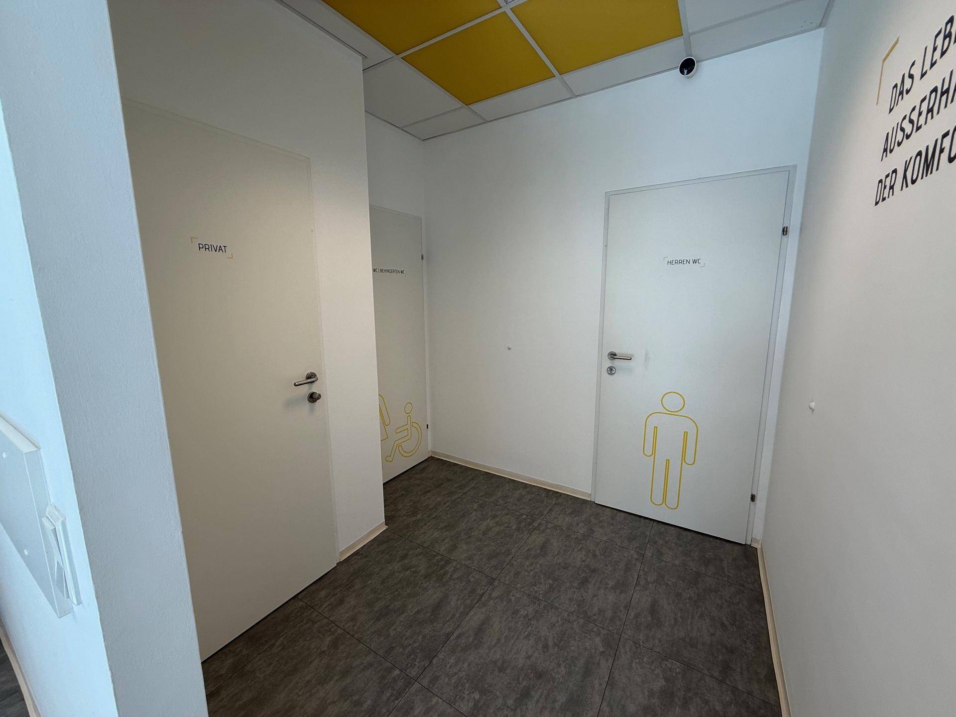 Flur mit Zugang zu verschiedenen Toiletten, gekennzeichnet für Damen und Herren.