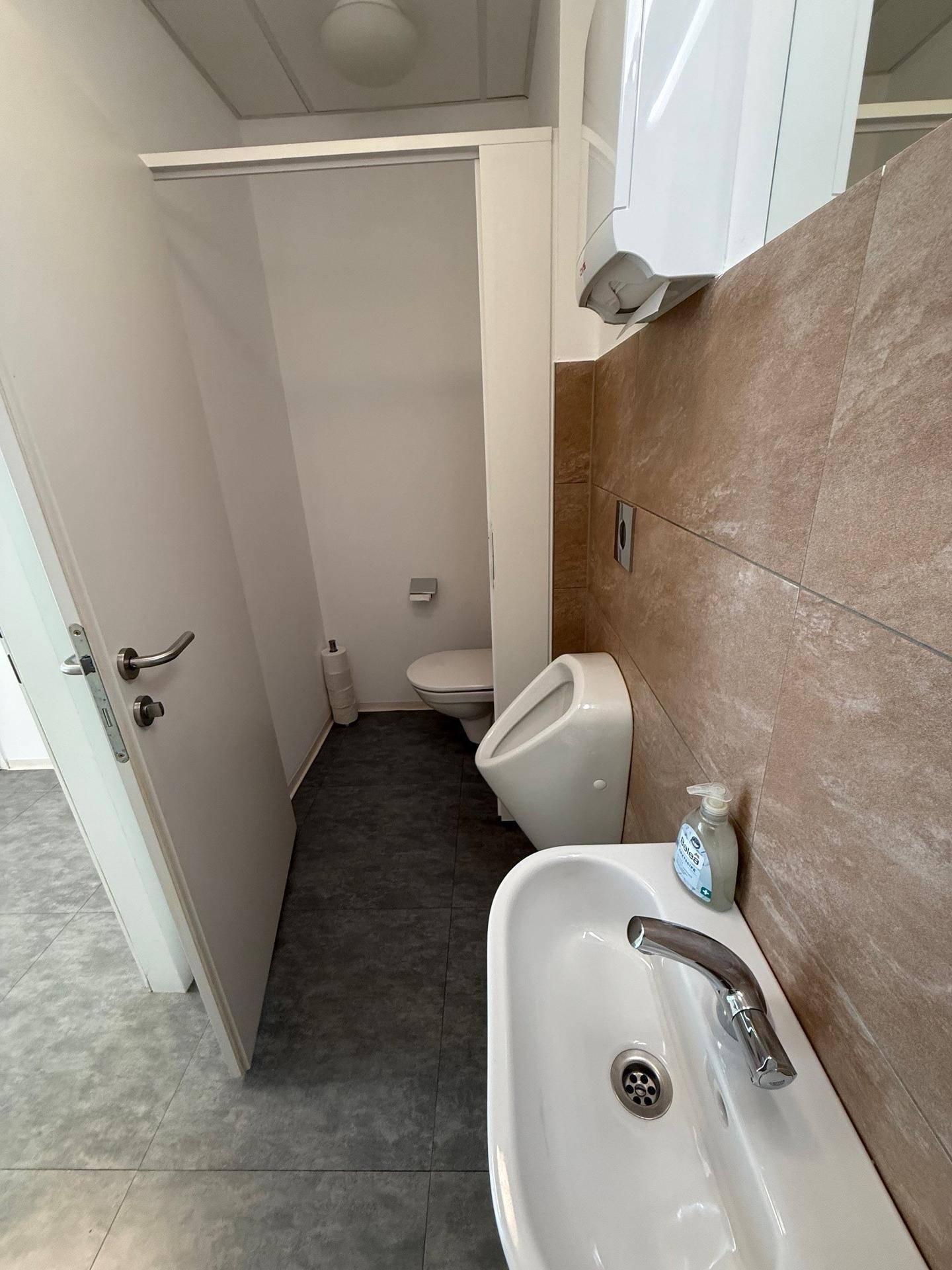 Herren-WC mit Urinal, Waschbecken und Wand-WC, sauber und funktional eingerichtet.