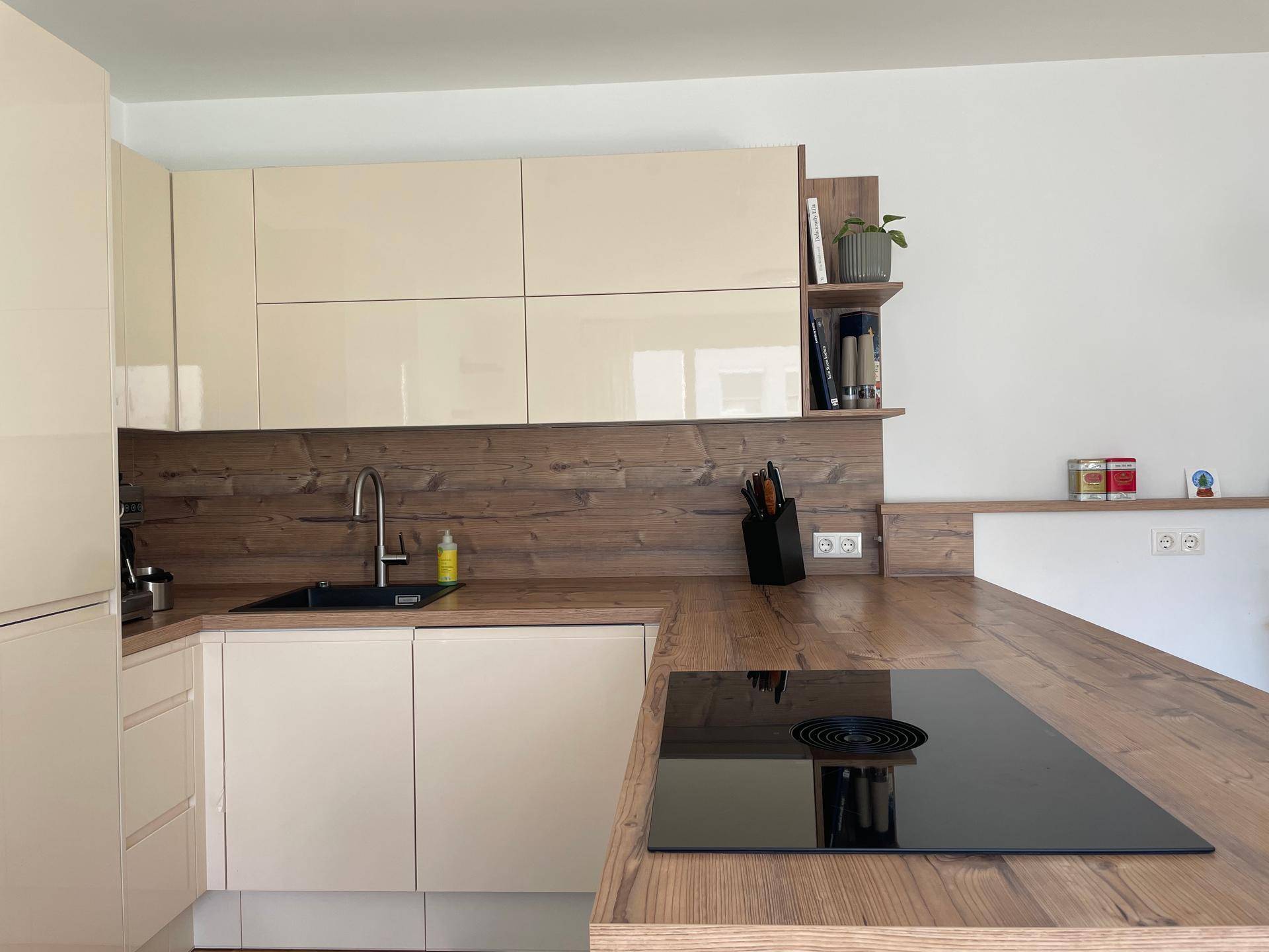 Moderne Küche mit beigen Hochglanzfronten, Holzarbeitsplatte und integriertem Induktionskochfeld.