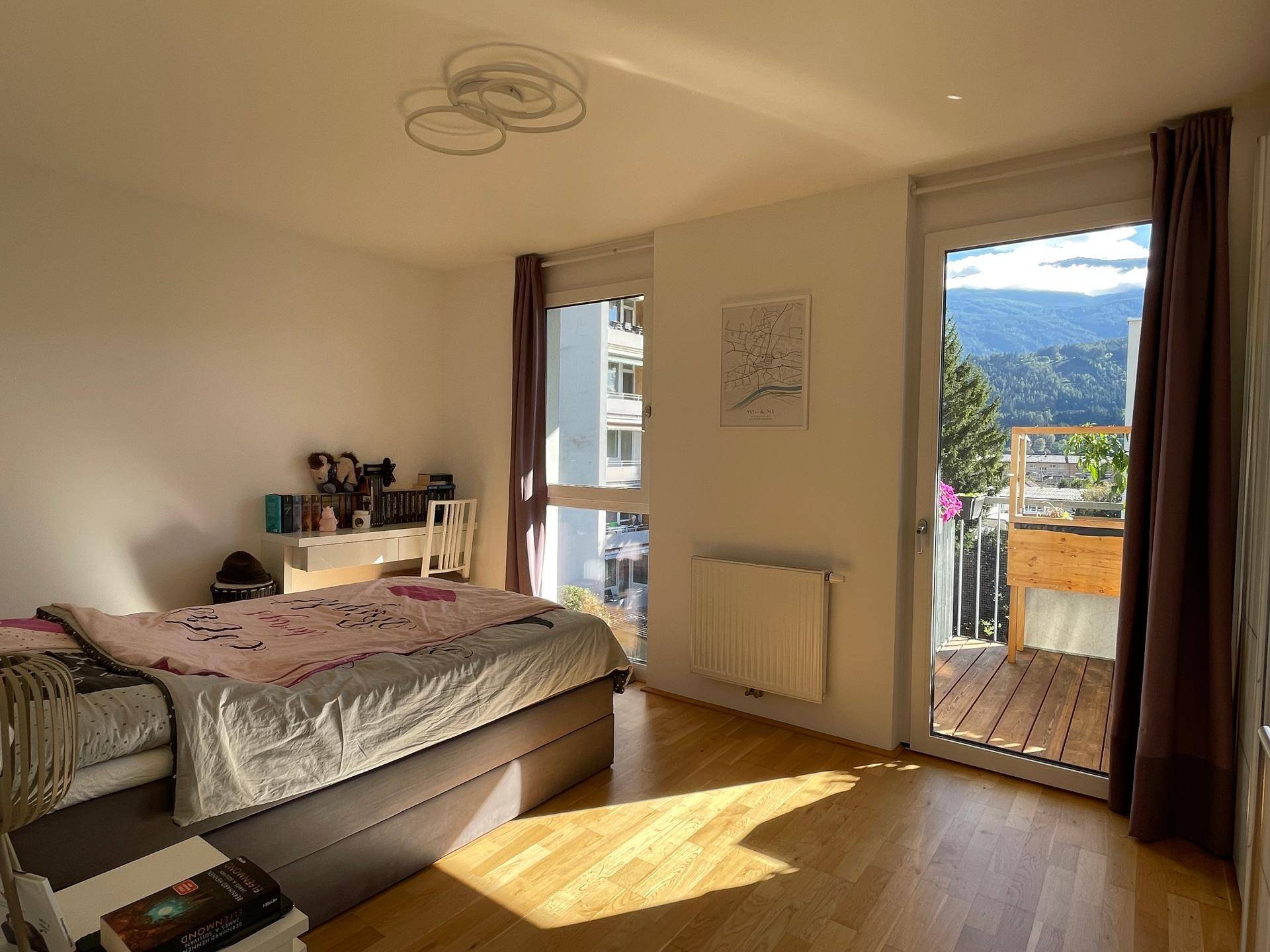 Sonniges Schlafzimmer mit Holzboden, Balkonzugang und weitem Blick auf die Berge.