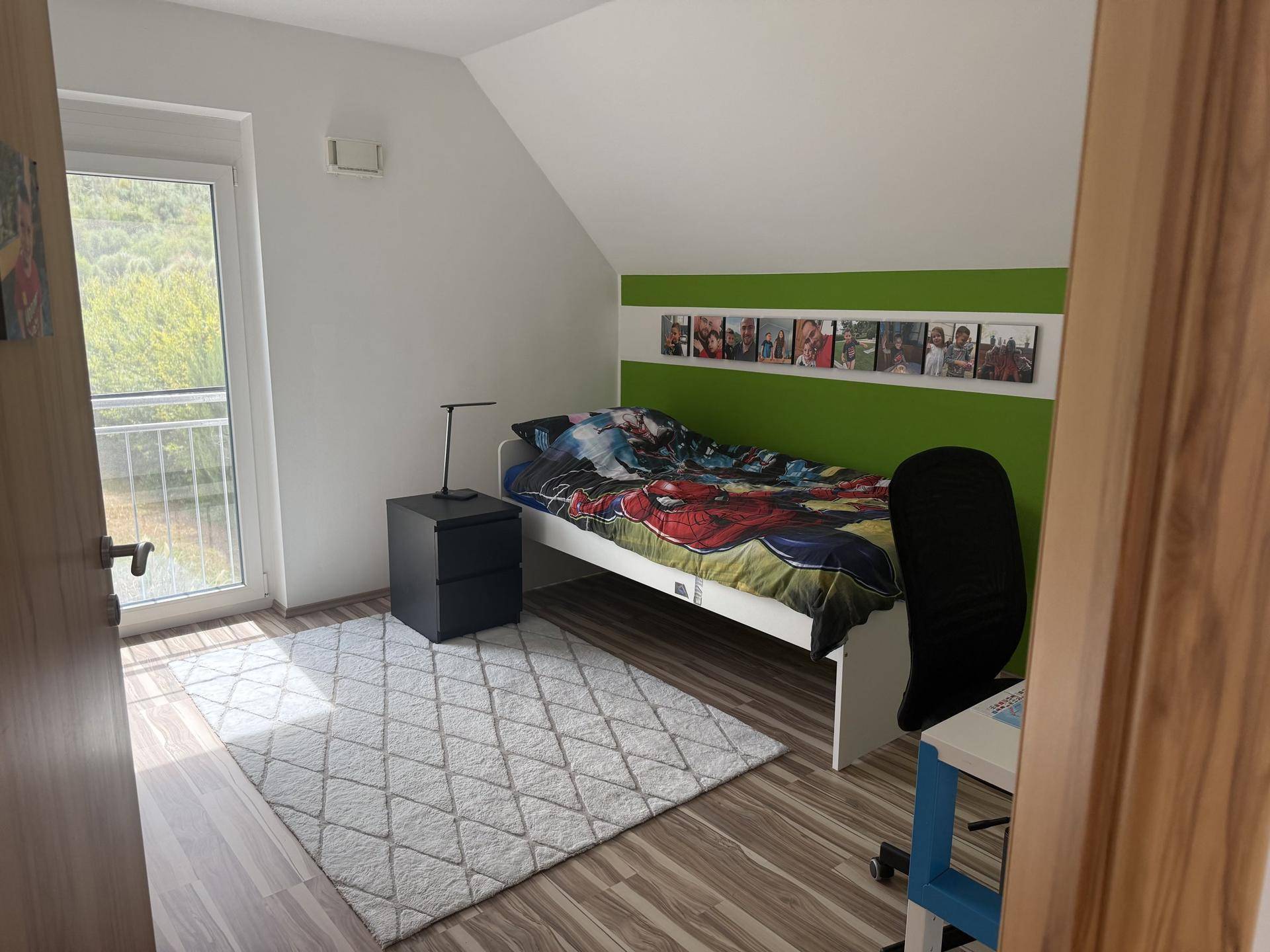 Helles Kinderzimmer mit Holzboden, grüner Akzentwand und Zugang zu einem französischen Balkon.