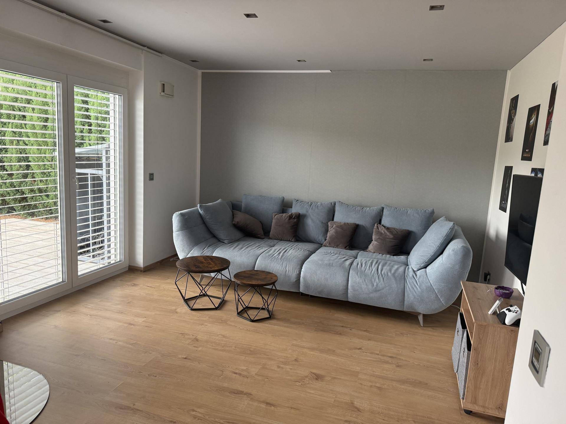Helles Wohnzimmer mit modernem Sofa, Holzboden und Zugang zur Terrasse durch große Fenster.