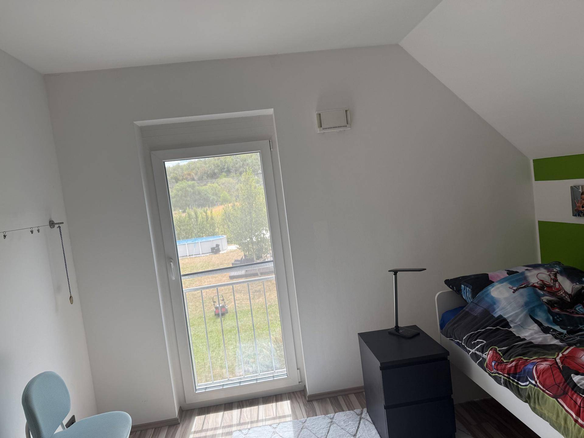 Schlafzimmer mit schrägen Wänden, Holzboden und Blick ins Grüne durch die Balkontür.