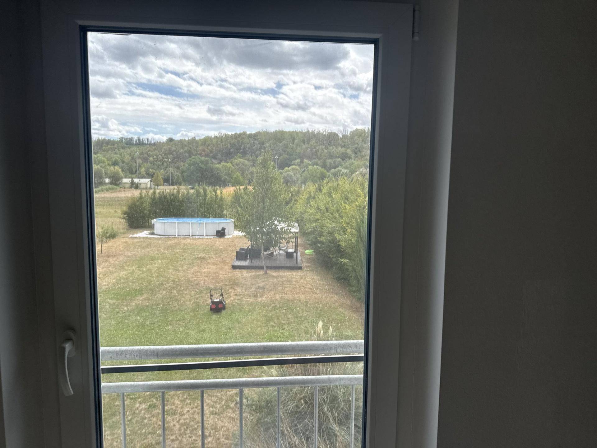 Blick aus dem Fenster auf den weitläufigen Garten mit Pool und grüner Landschaft im Hintergrund.