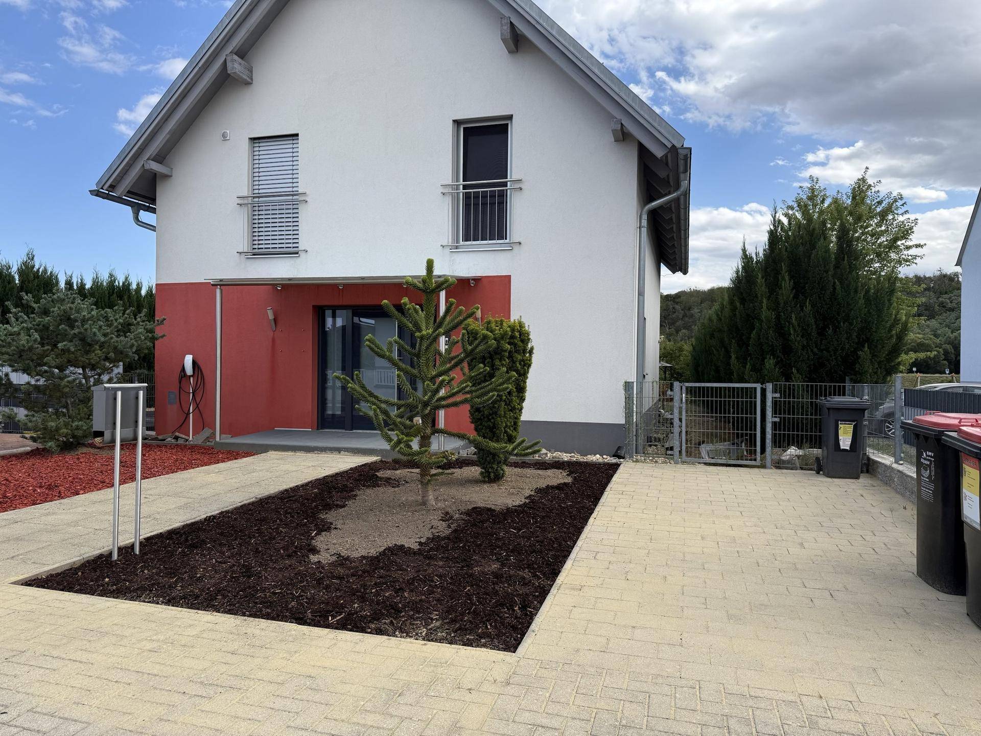 Vorderansicht des Einfamilienhauses mit weißer und roter Fassade, Vorgarten und gepflasterter Einfahrt.