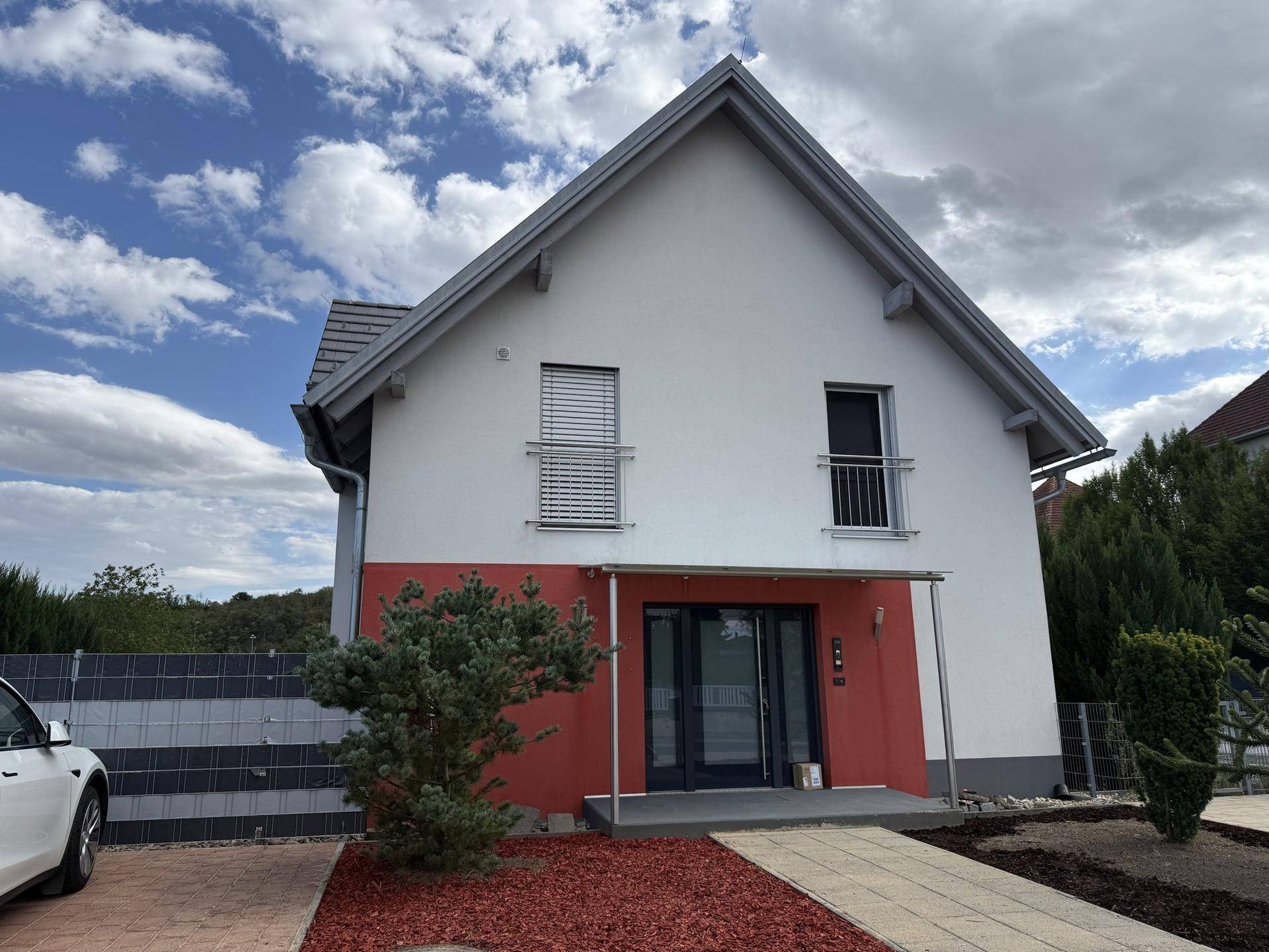Ansicht des modernen Einfamilienhauses mit weißer und roter Fassade, Vorgarten und gepflastertem Weg.
