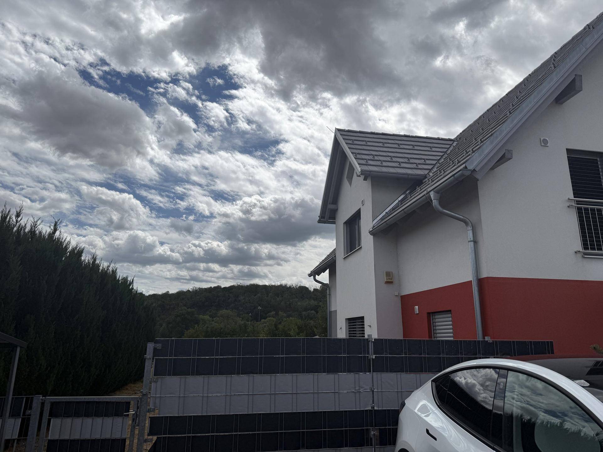 Seitenansicht des modernen Hauses mit Zaun und einem geparkten Elektrofahrzeug im Vordergrund.