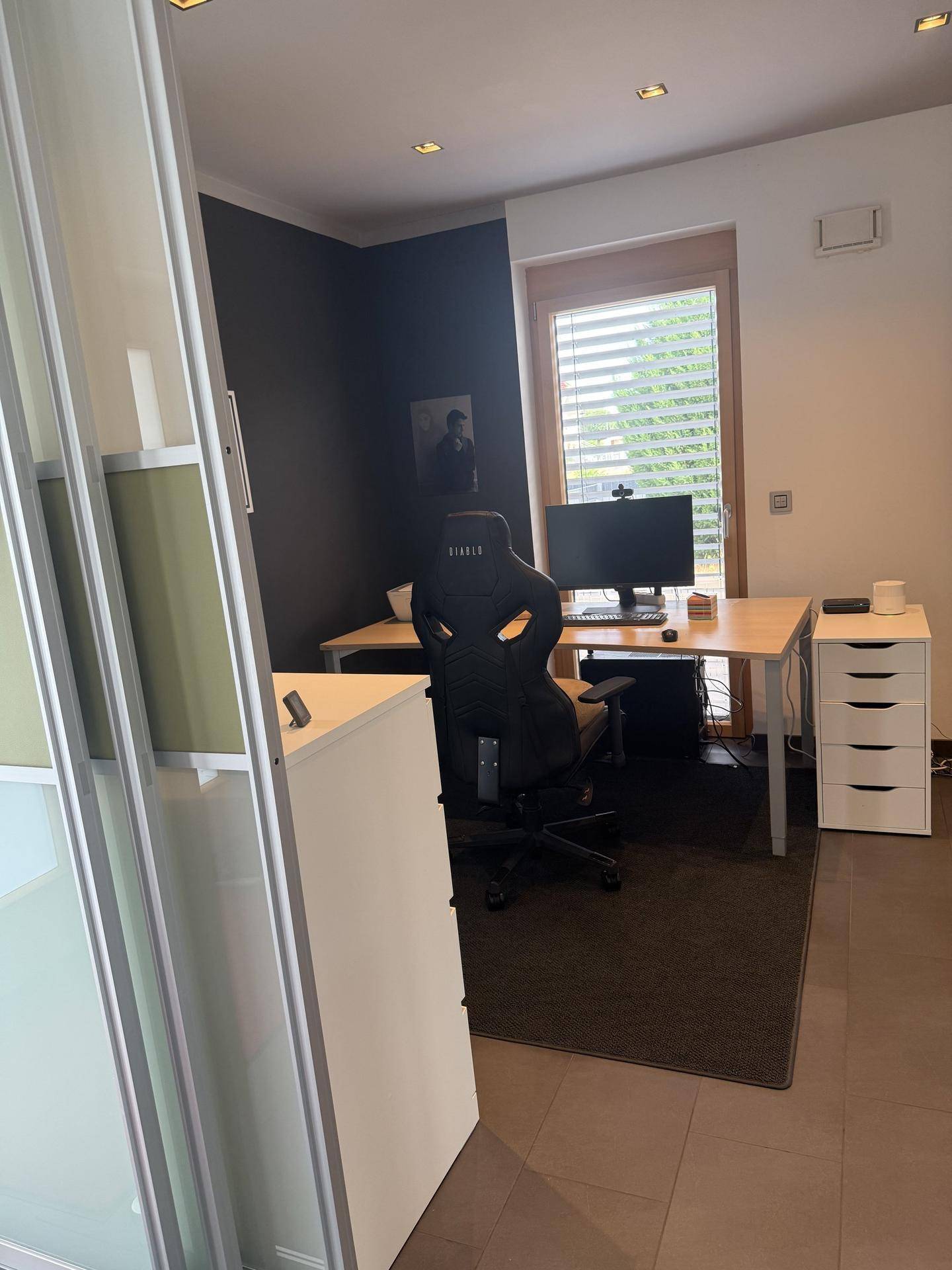 Modernes Arbeitszimmer mit Schreibtisch, Bürostuhl und großem Fenster mit Jalousien.
