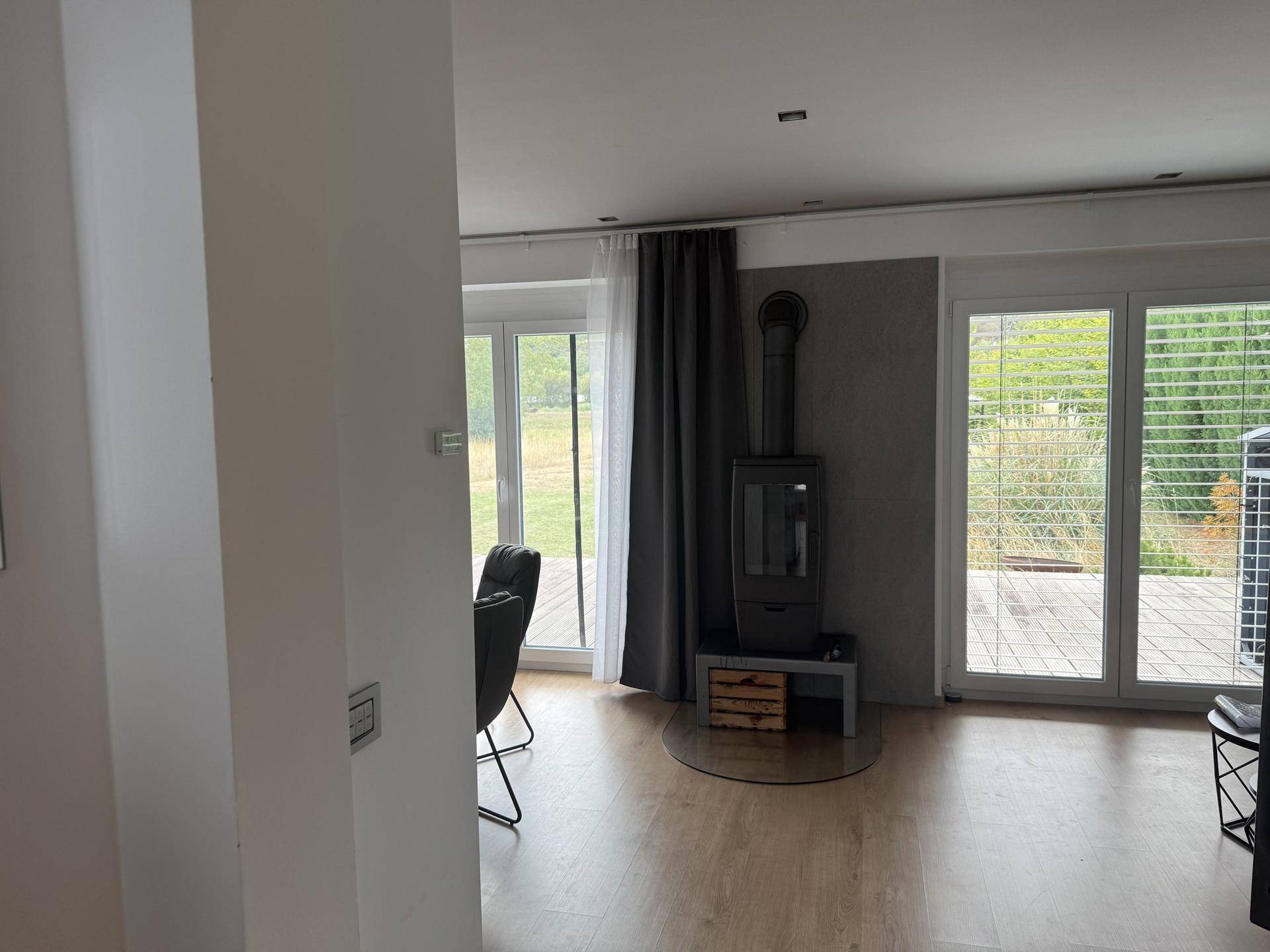 Geräumiges Wohnzimmer mit Holzboden, Kaminofen und großen Fenstern zum Garten.