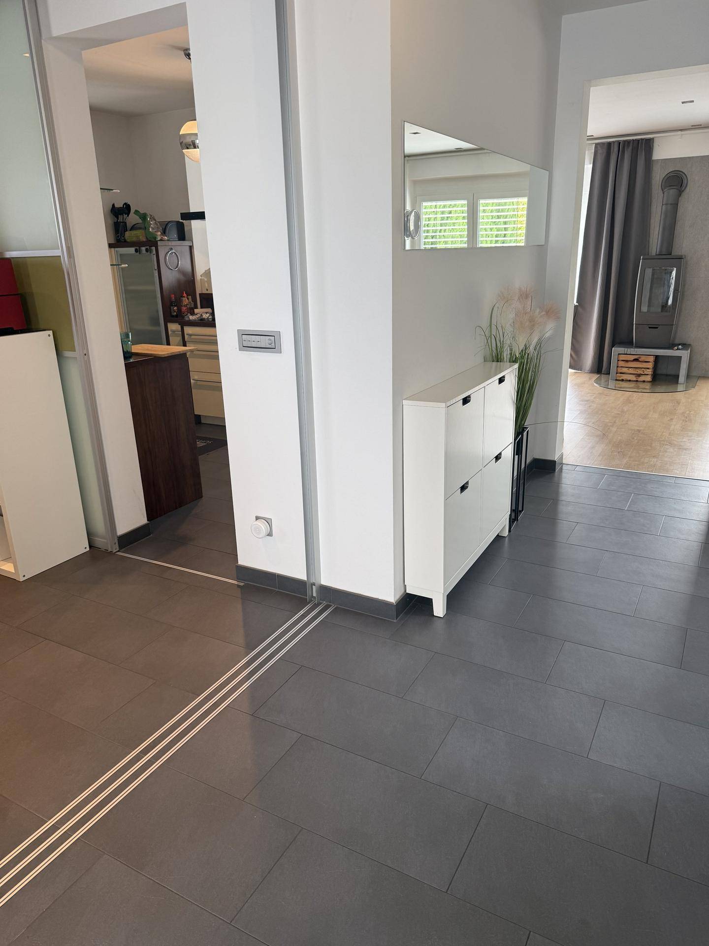 Flur mit dunklen Fliesen, Schuhschrank und Blick in den offenen Wohn-Essbereich.