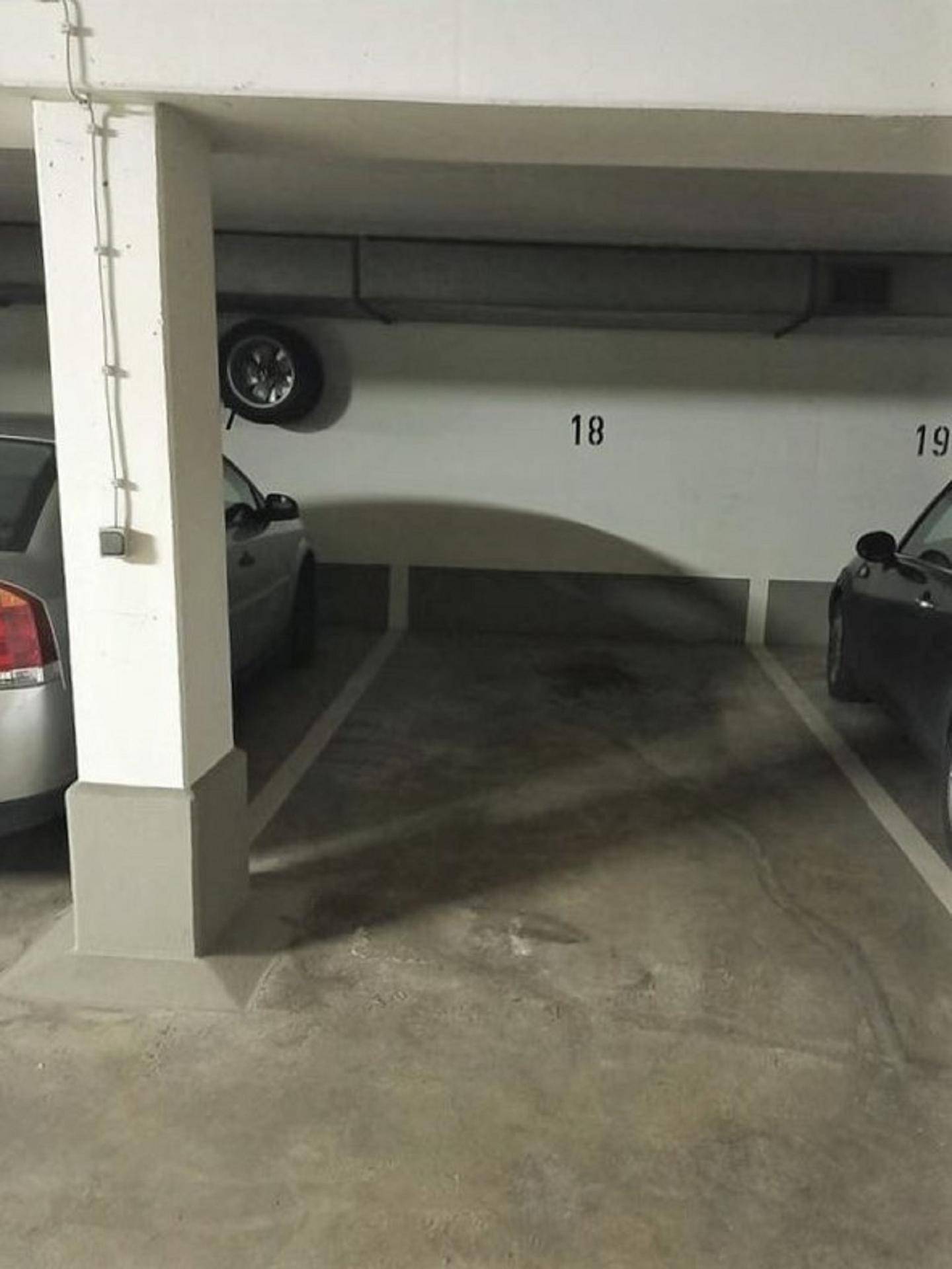 Tiefgarage mit nummerierten Parkplätzen, Betonstützen und einem an der Wand gelagerten Reifen.