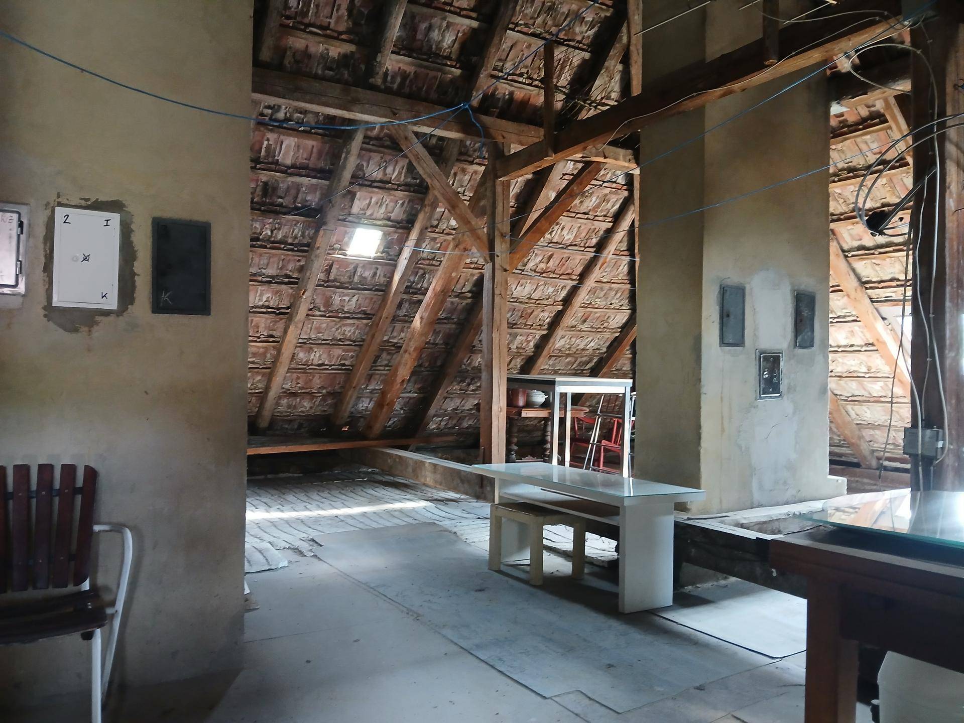 Unausgebauter Dachboden mit sichtbaren Holzbalken, Dachziegeln und einem Dachfenster.