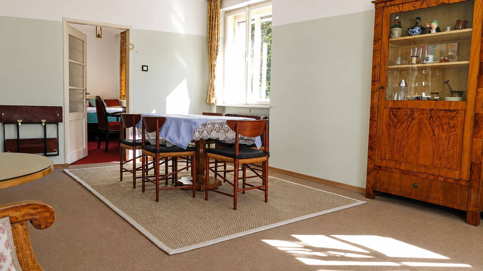 Klassisches Esszimmer mit Holztisch, Vitrine und Zugang zu einem weiteren Zimmer.