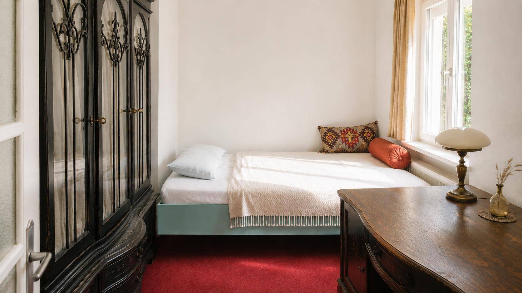 Kleines Schlafzimmer mit Einzelbett, dunklem Kleiderschrank und Fenster für Tageslicht.
