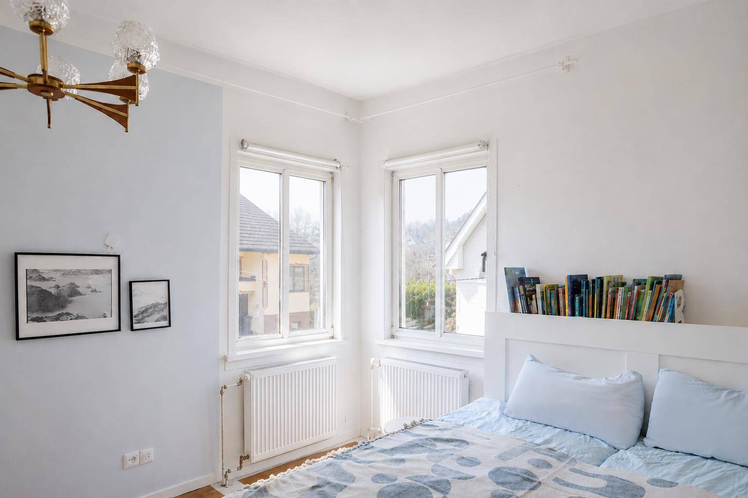 Gemütliches Schlafzimmer mit zwei Fenstern, einem Bett und integriertem Bücherregal.