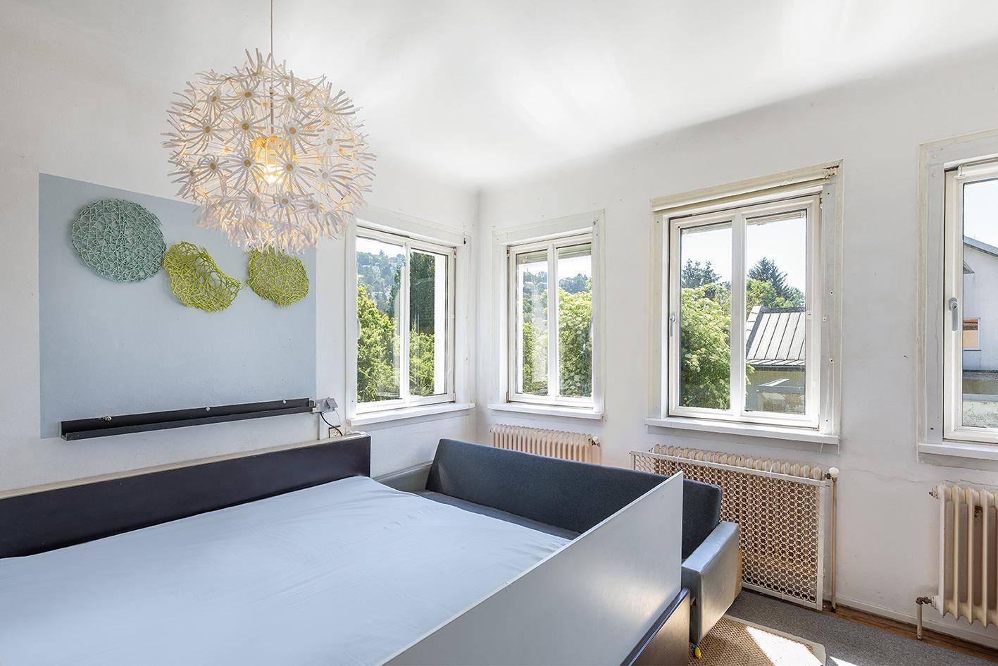 Helles Schlafzimmer mit mehreren Fenstern, einem Bett und einer modernen Deckenleuchte.