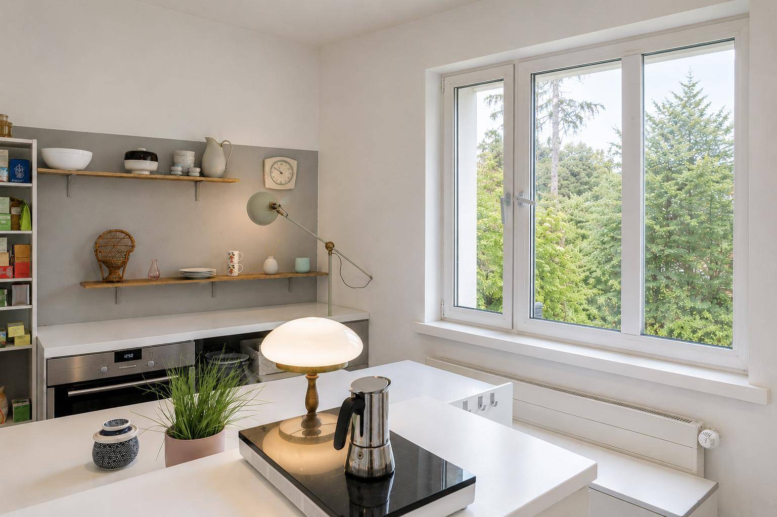 Helle Küche mit weißen Arbeitsplatten, offenen Regalen und großem Fenster mit Waldblick.