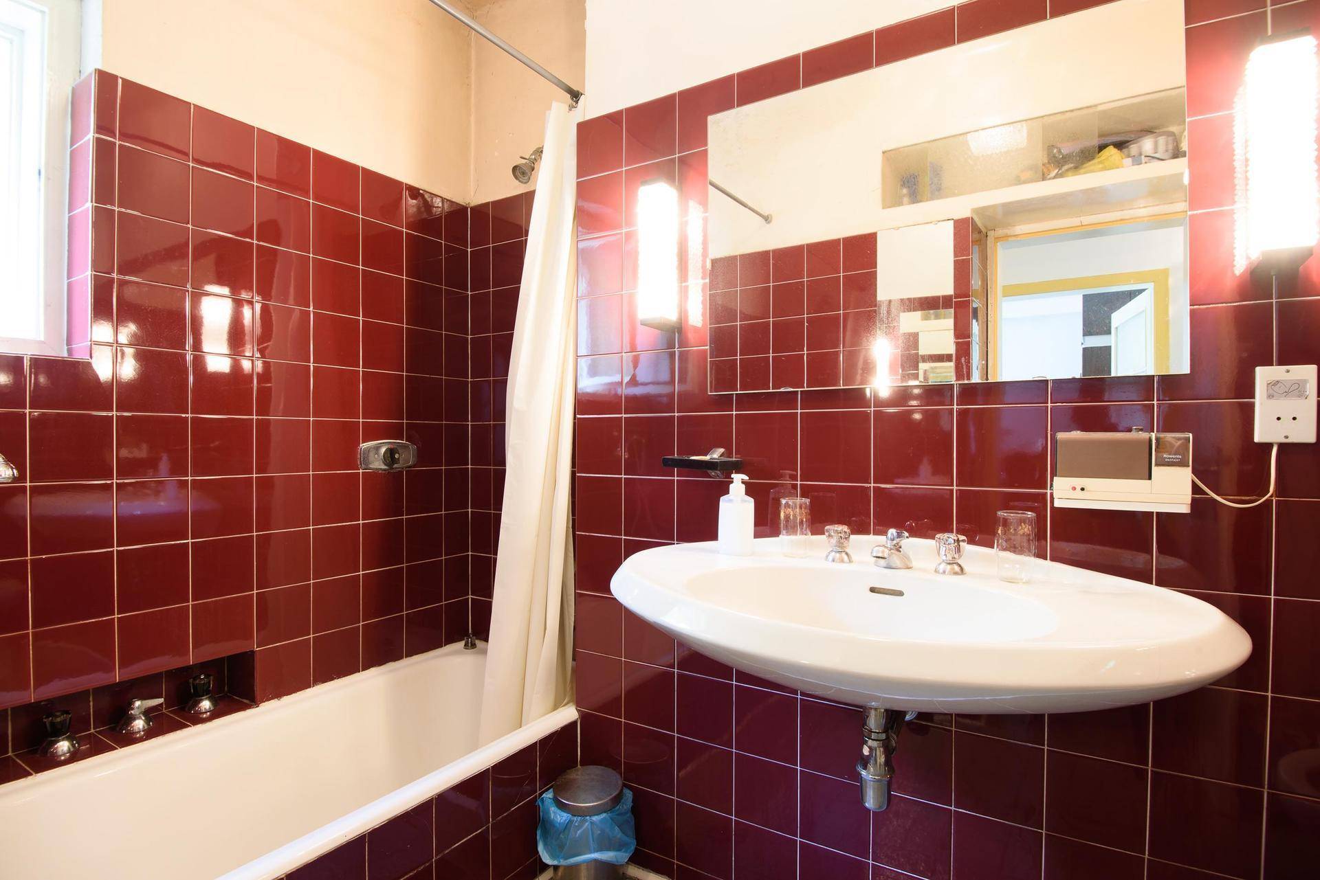 Badezimmer mit roten Fliesen, Badewanne mit Duschvorhang und Waschbecken.