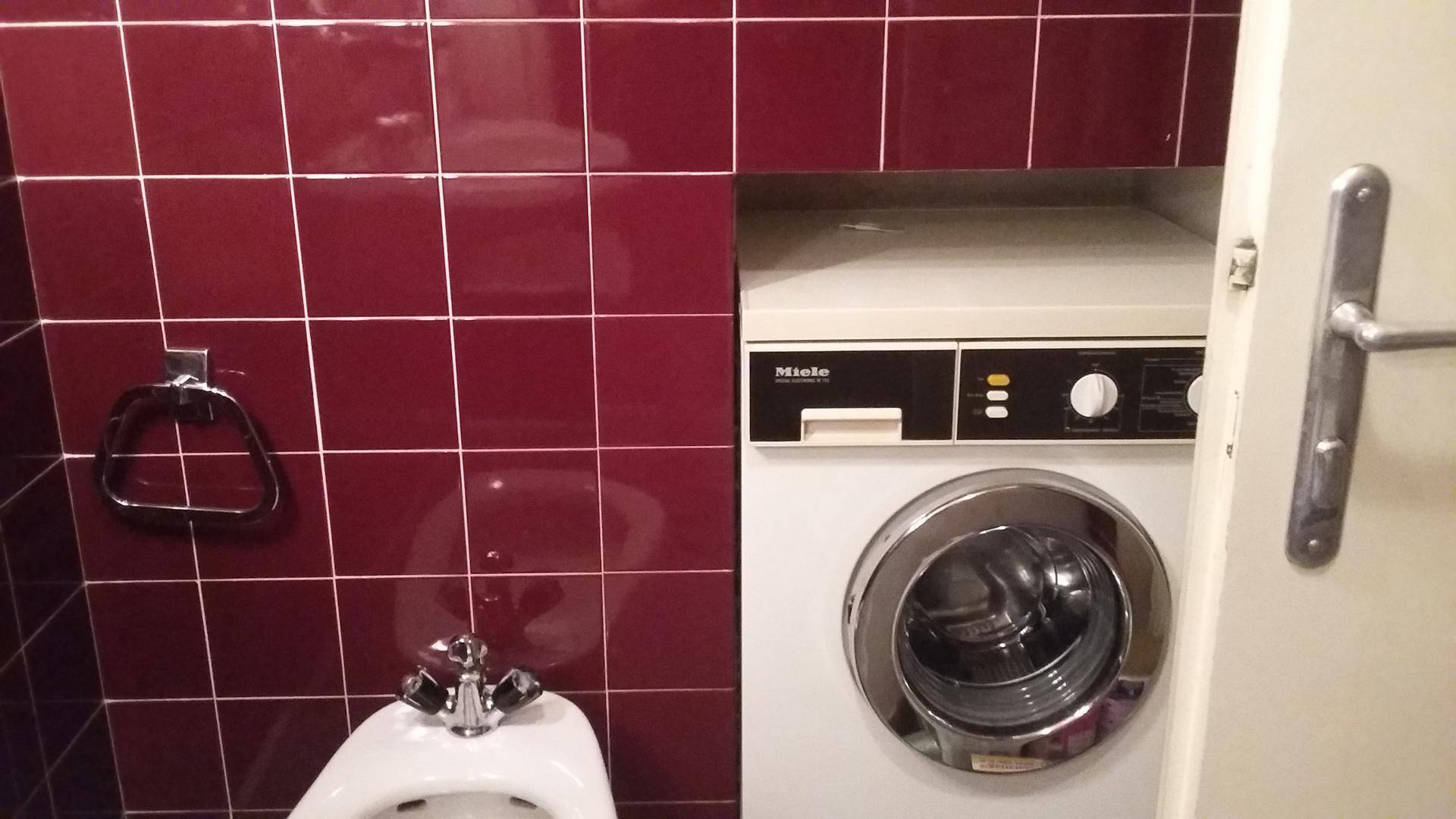 Badezimmer mit roten Fliesen, Bidet und integrierter Waschmaschine.