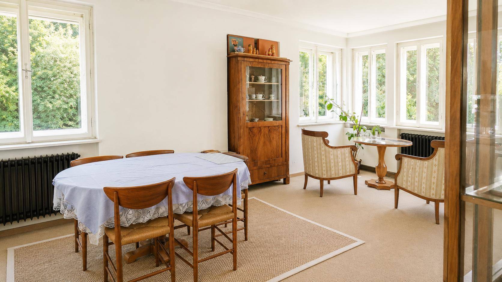 Geräumiges Esszimmer mit großem Holztisch, Vitrine und vielen Fenstern für viel Tageslicht.