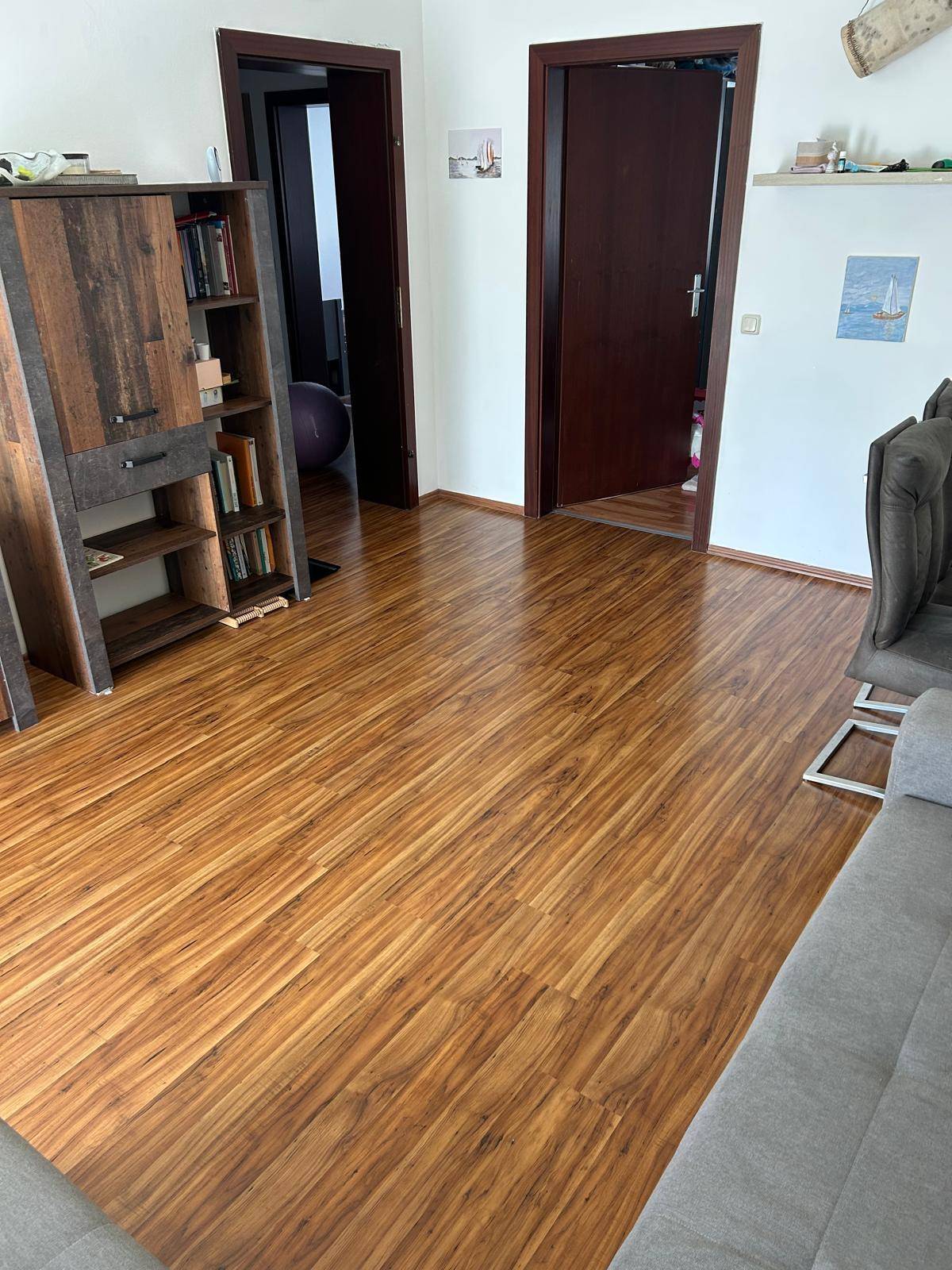 Wohnbereich mit glänzendem Laminatboden und dunklen Holztüren, die zu weiteren Räumen führen.