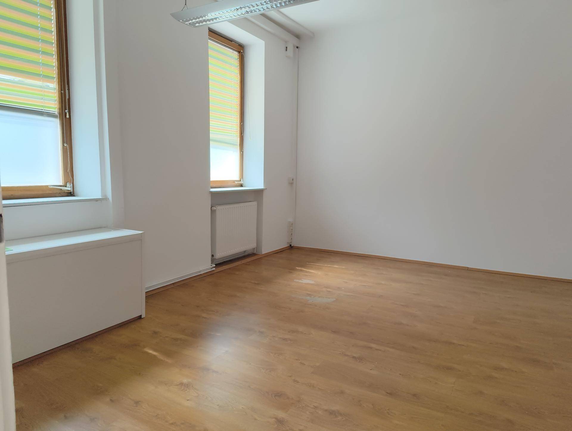 Leerer Raum mit zwei Fenstern, Heizkörpern und hellem Laminatboden, bereit zur individuellen Nutzung.