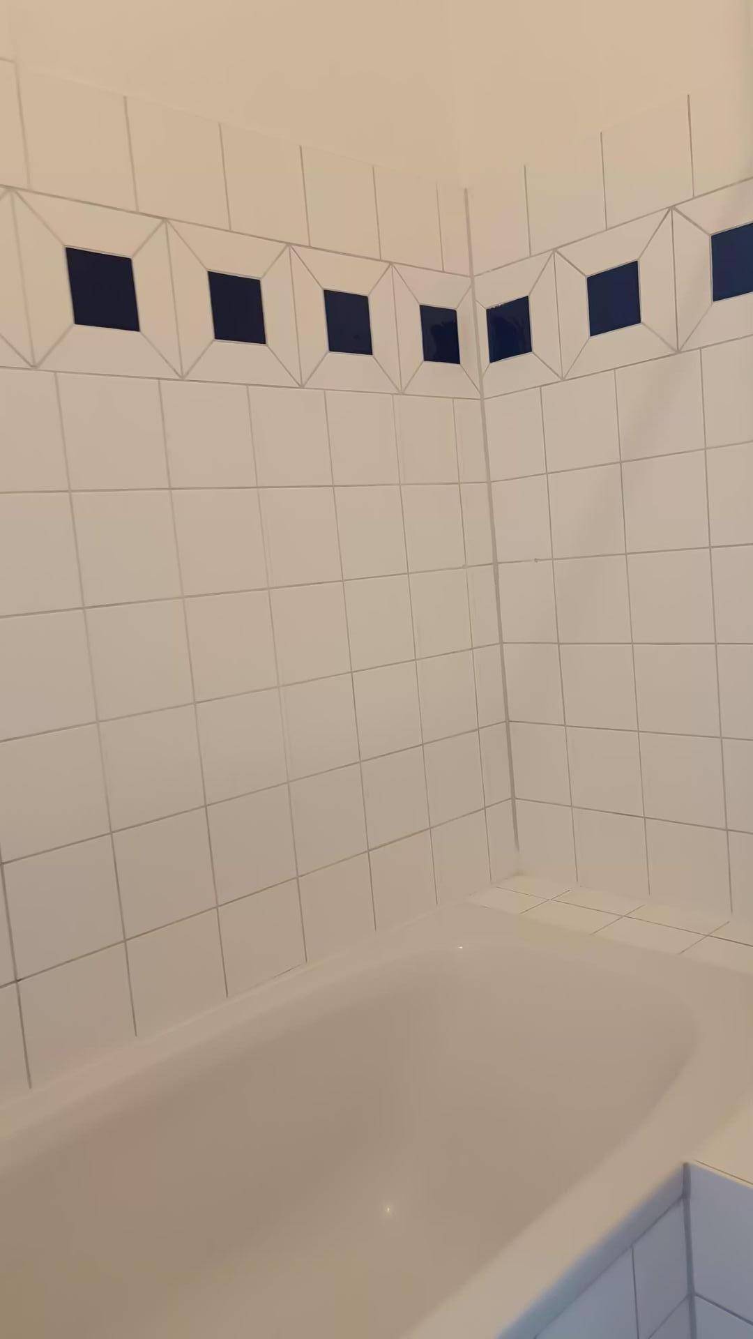 Badewanne in einem Badezimmer mit weißen Fliesen und blauen Dekorelementen.