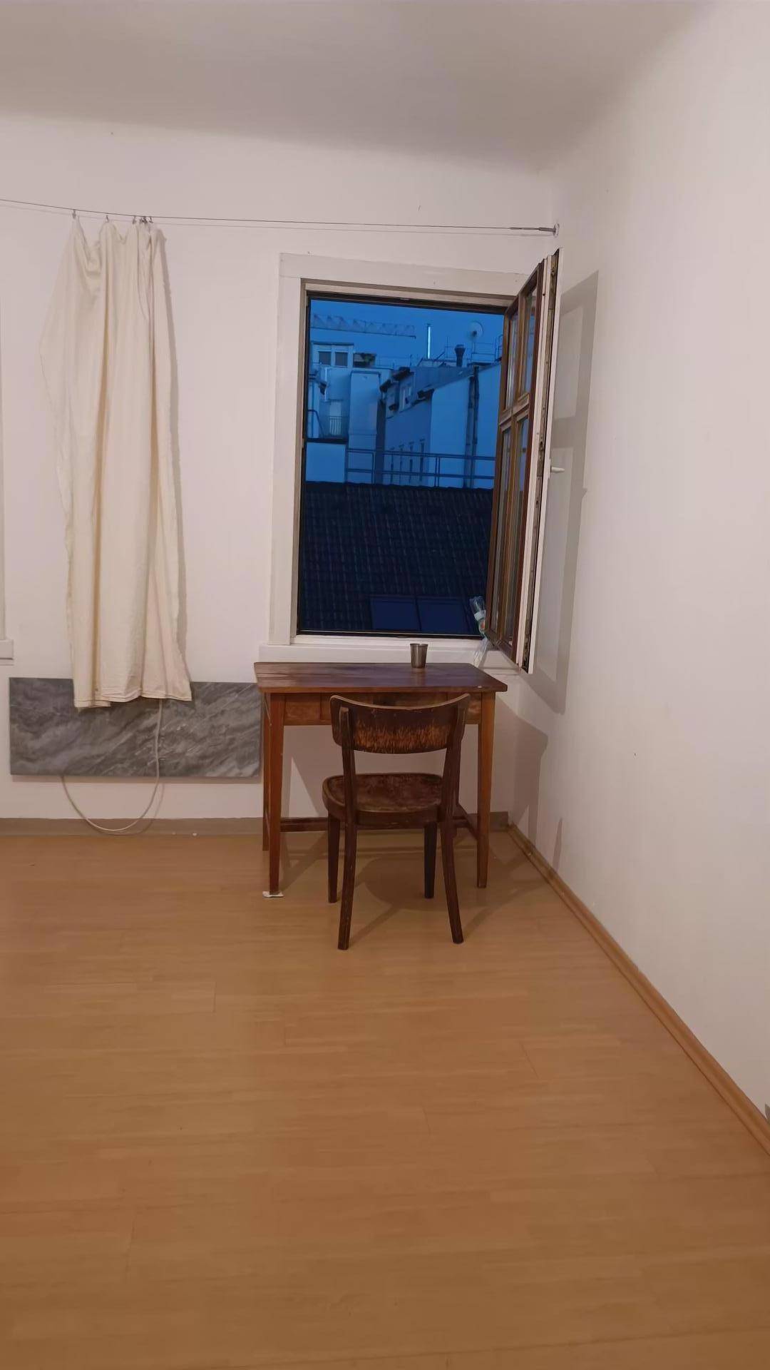 Leerer Raum mit hellem Holzfußboden, weiß gestrichenen Wänden und einem geöffneten Fenster.