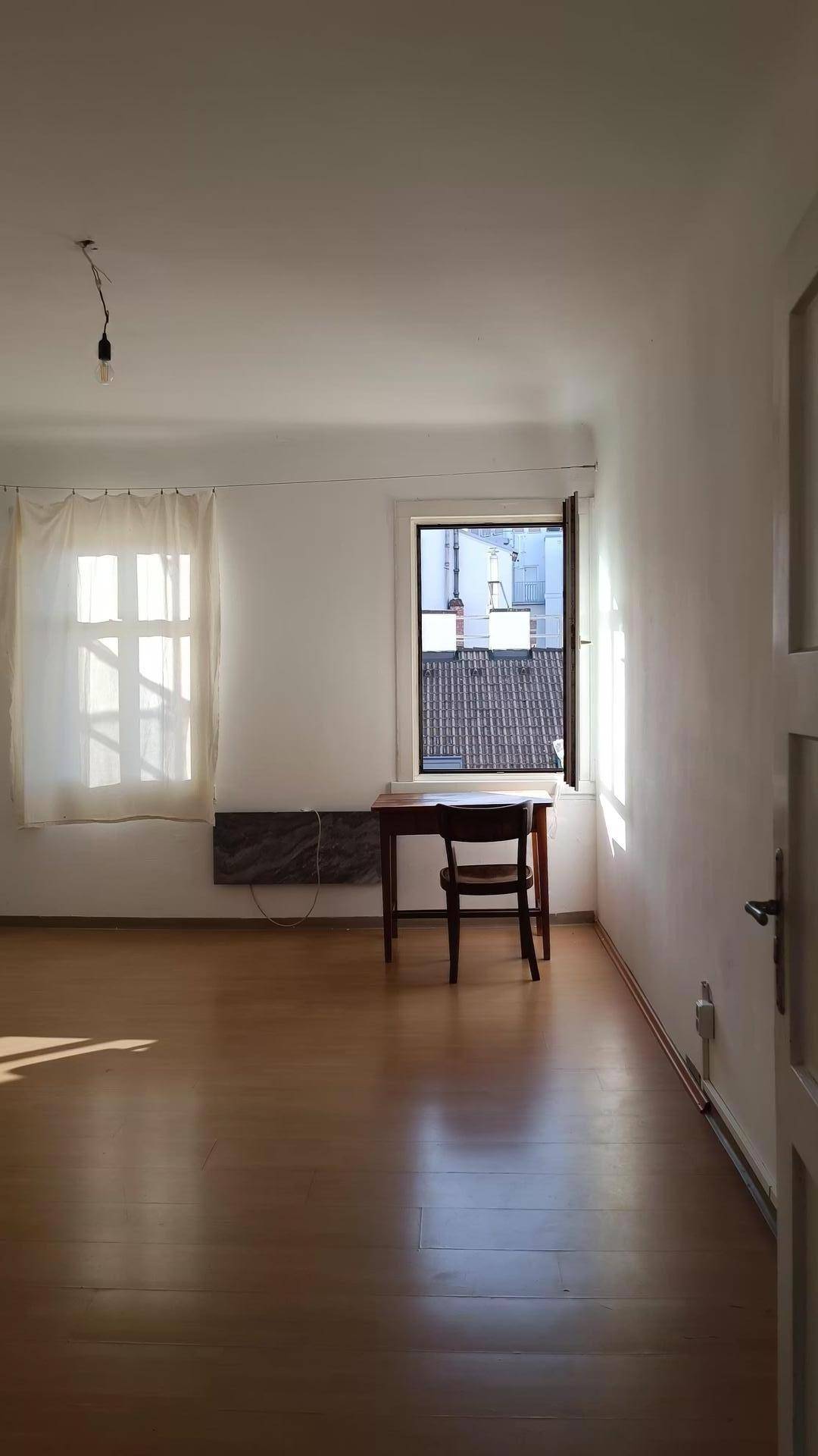 Heller Raum mit Holzfußboden und großem Fenster, das viel Tageslicht hereinlässt.