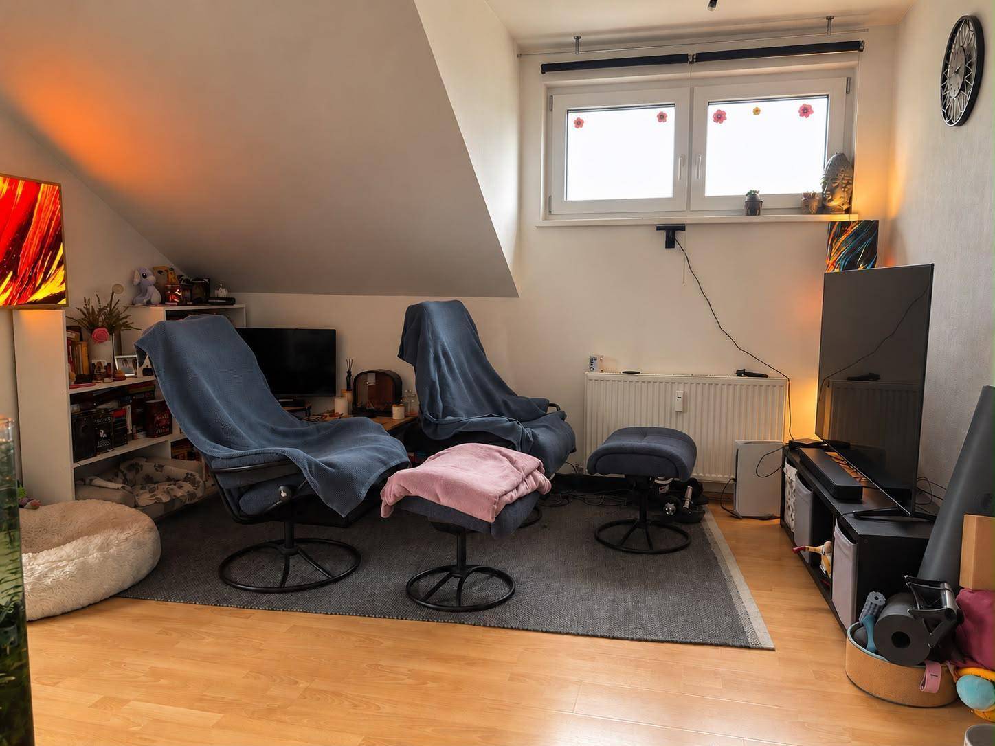 Wohnbereich mit bequemen Sesseln, Fernseher und einem Fenster unter der Dachschräge.